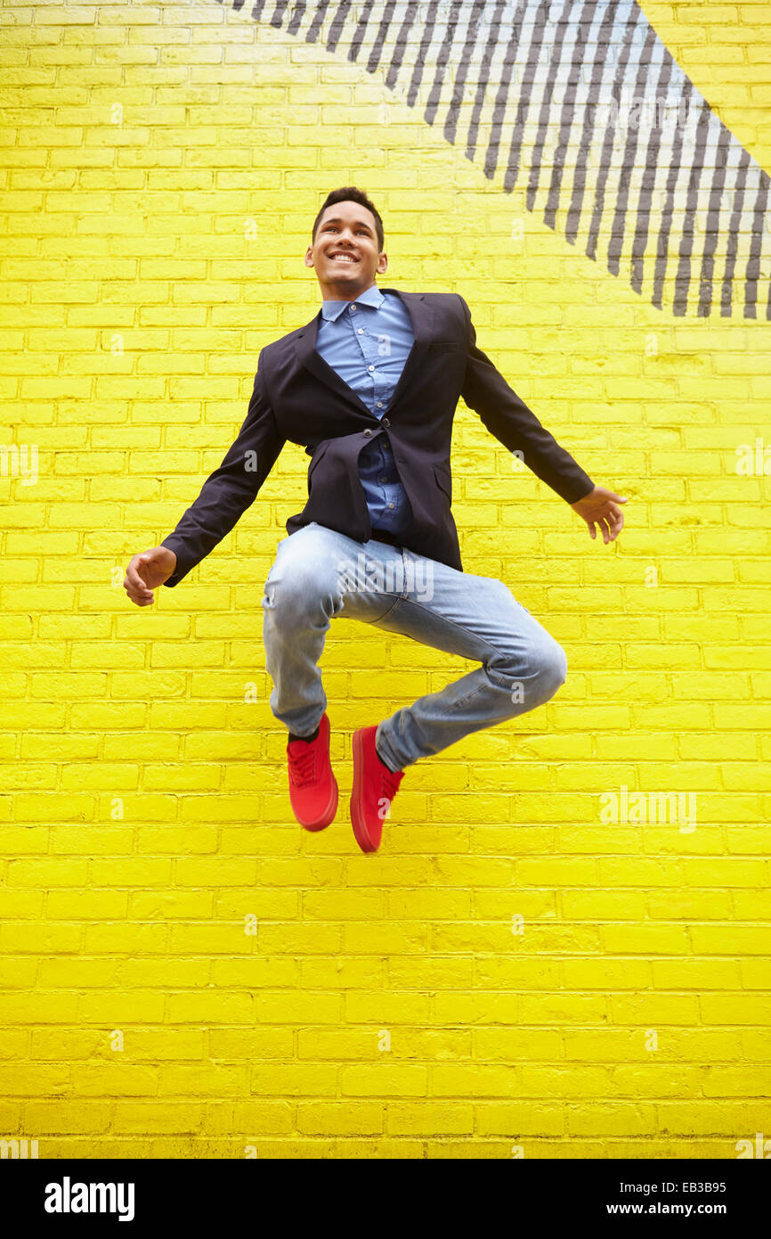 Uomo sorridente salti di gioia nei pressi di colore giallo brillante parete Foto Stock
