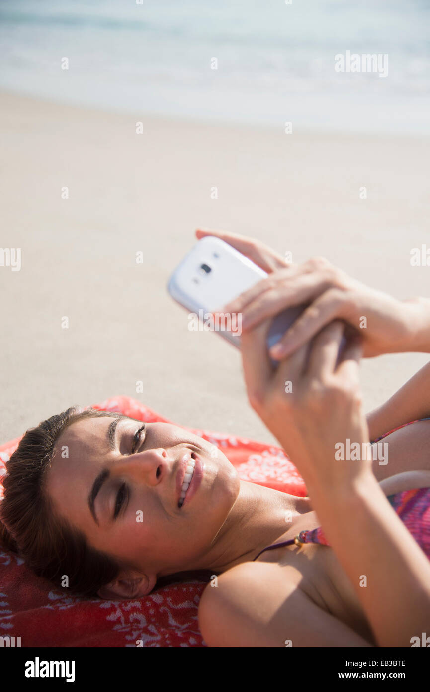 La donna caucasica tramite telefono cellulare sulla spiaggia Foto Stock