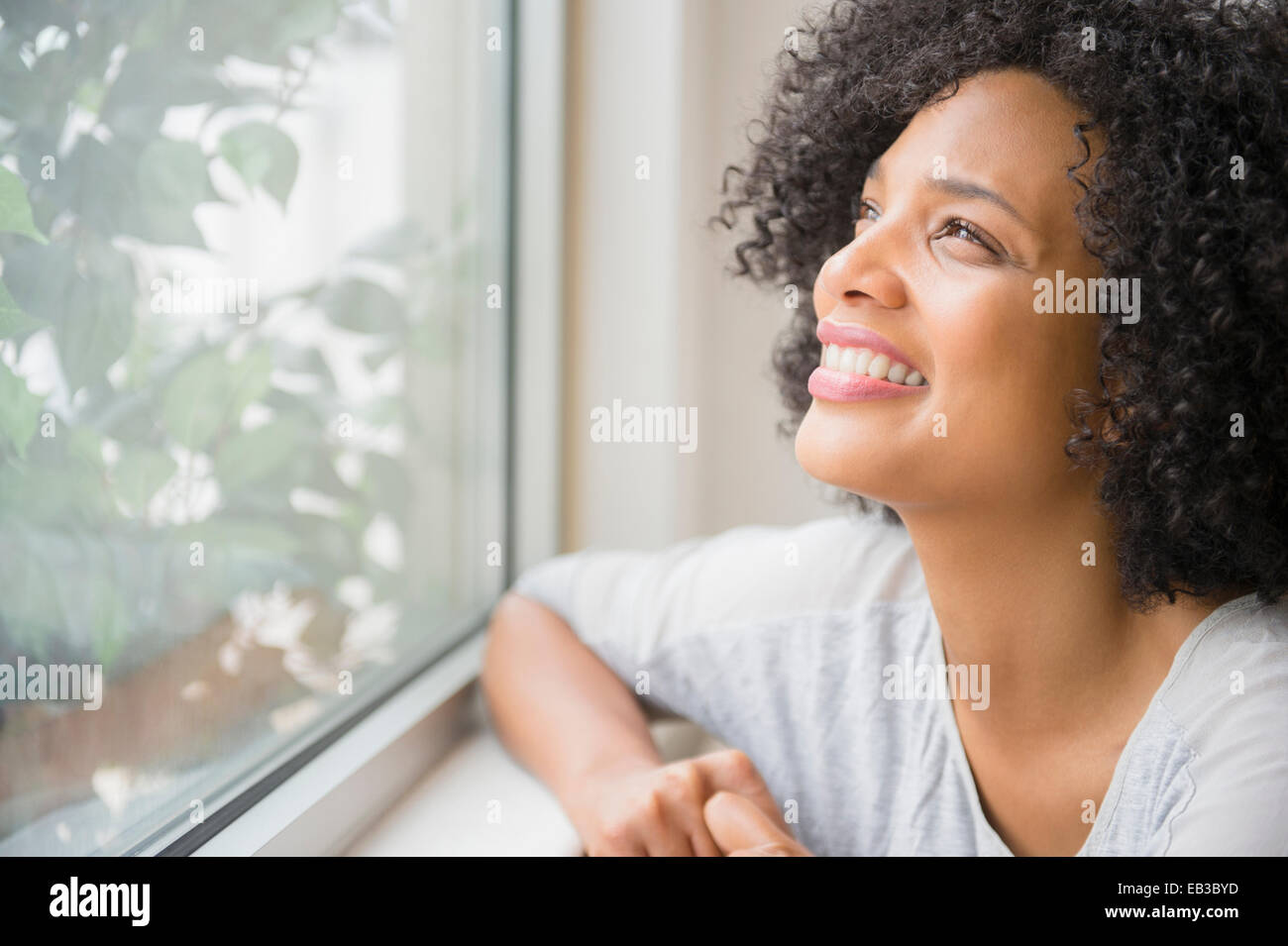 Donna sorridente a guardare fuori dalla finestra Foto Stock