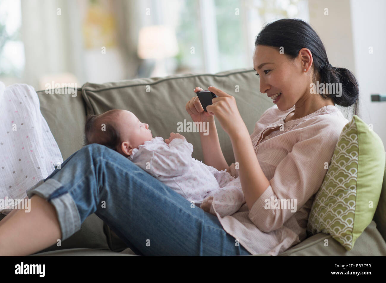 Asian madre assunzione cellulare fotografia del bambino nella stanza vivente Foto Stock