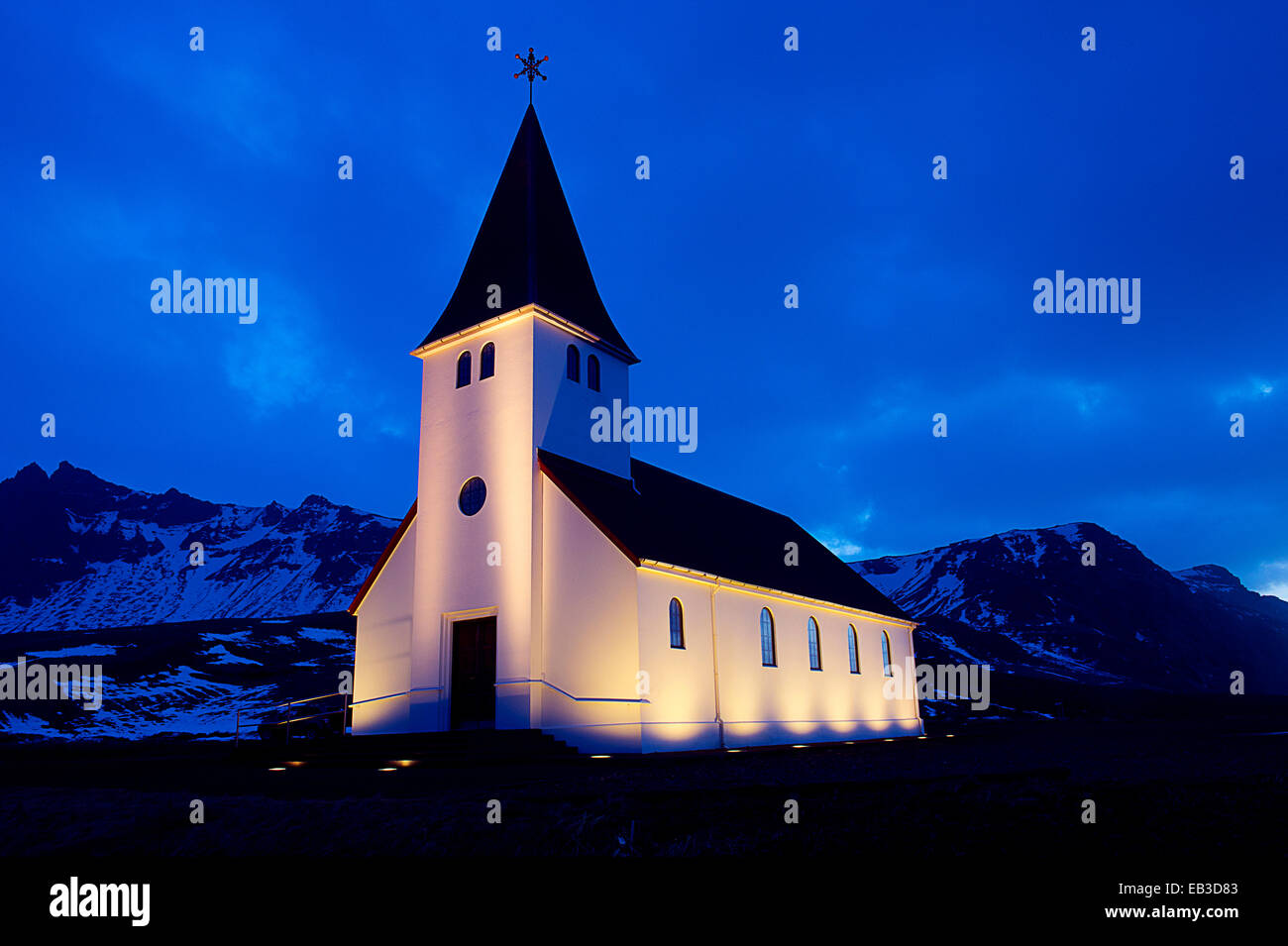 Chiesa bianca accesa vicino a montagne innevate di notte Foto Stock