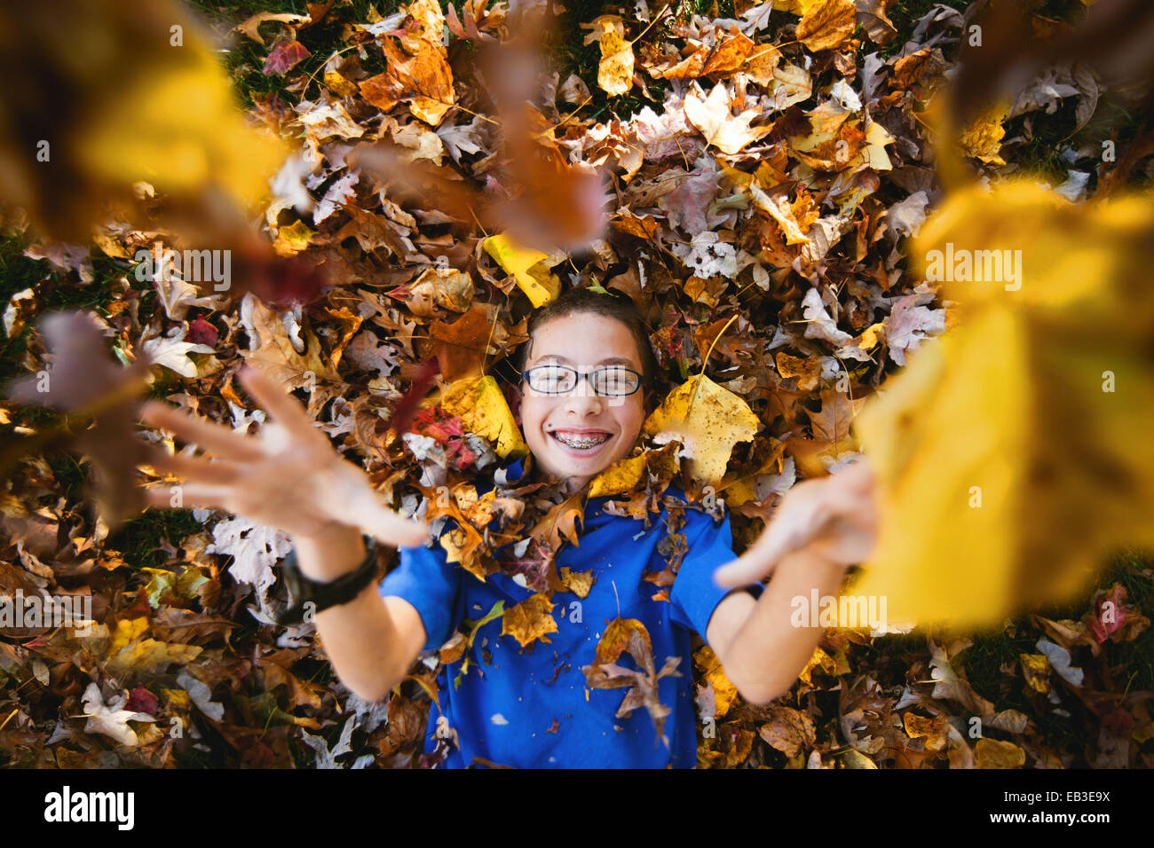 Ragazzo sdraiato sulla schiena giocando con foglie d'autunno Foto Stock