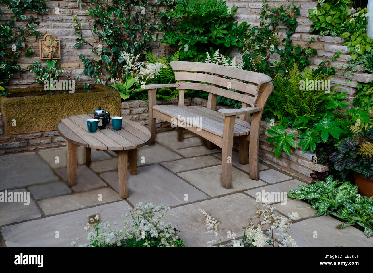 Close up di un giardino in legno sedile e tabella in un giardino murato patio Foto Stock