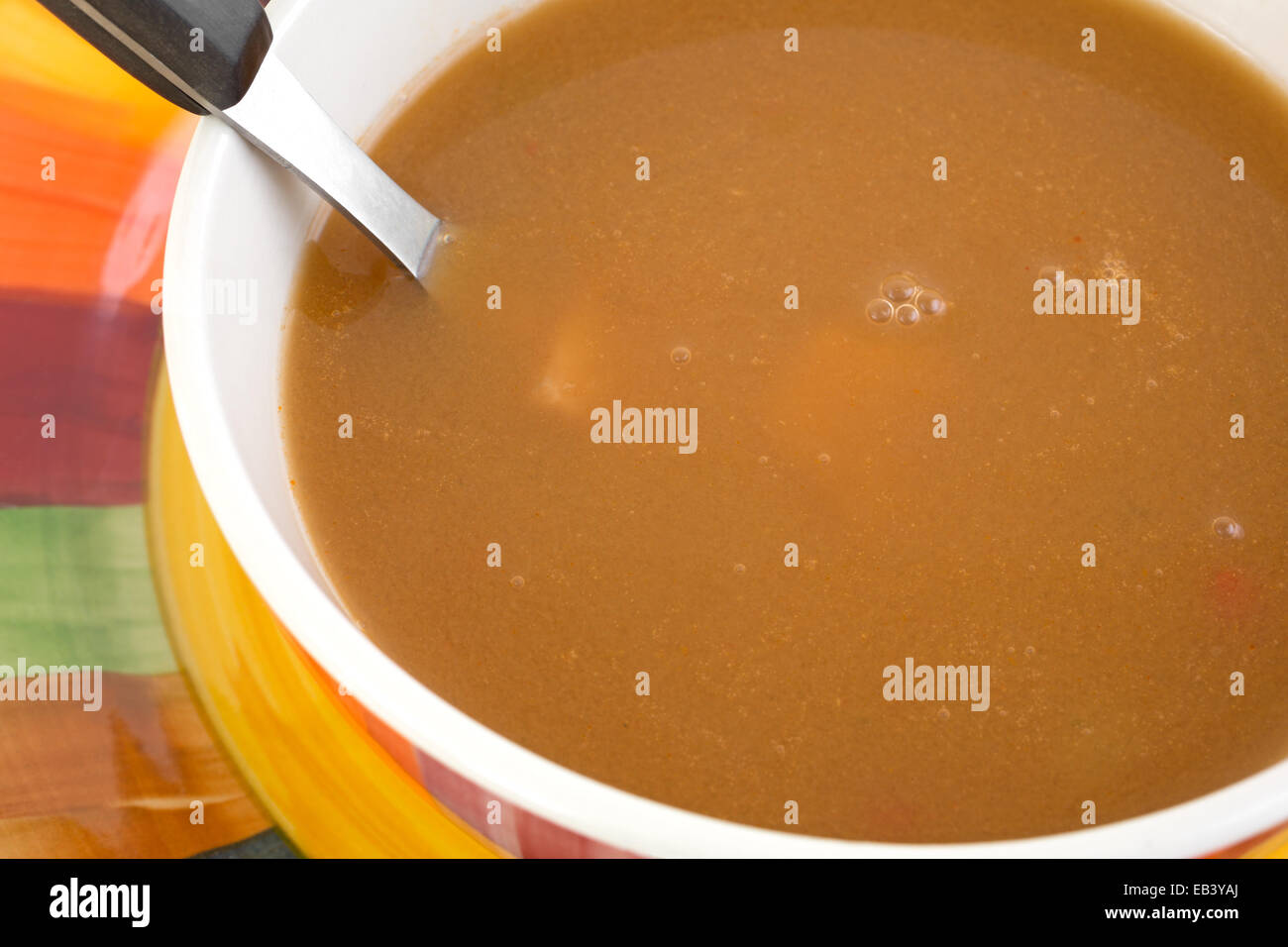 Una ciotola di zuppa di pollo in brodo di pomodoro con cucchiaio su una piastra colorati. Foto Stock