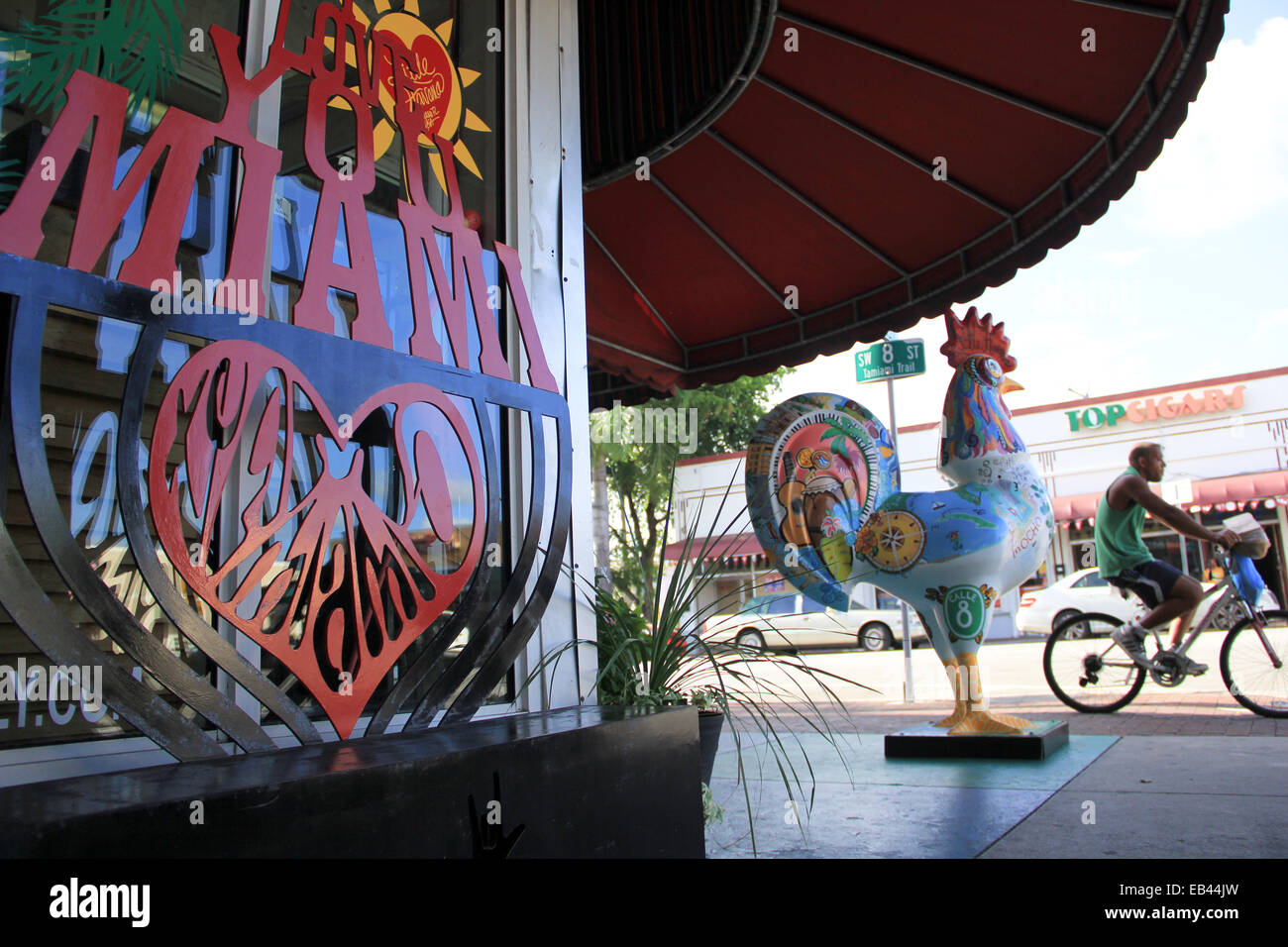 Un ciclista passa una scultura in legno di un gallo in Little Havana quartiere di Miami, Florida. Foto Stock