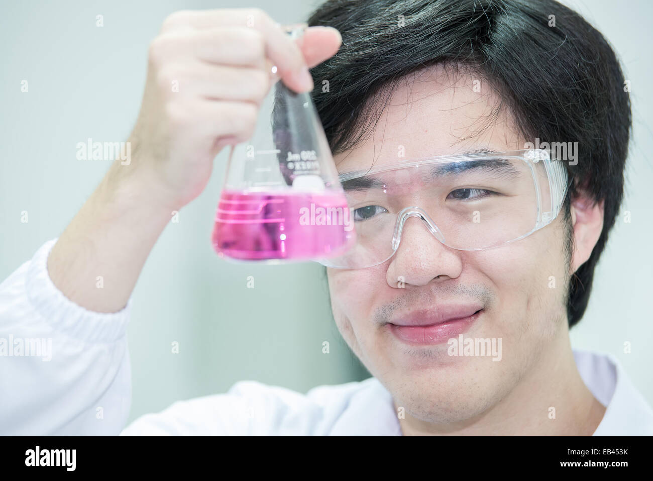 Scienziato asiatico in laboratorio, esamina una provetta con del liquido Foto Stock