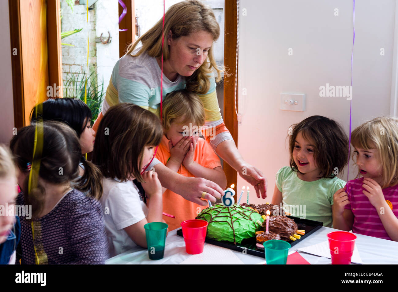Un ragazzo soffiando fuori le candele sulla sua torta presso la sua festa di compleanno circondato dai suoi amici. Foto Stock