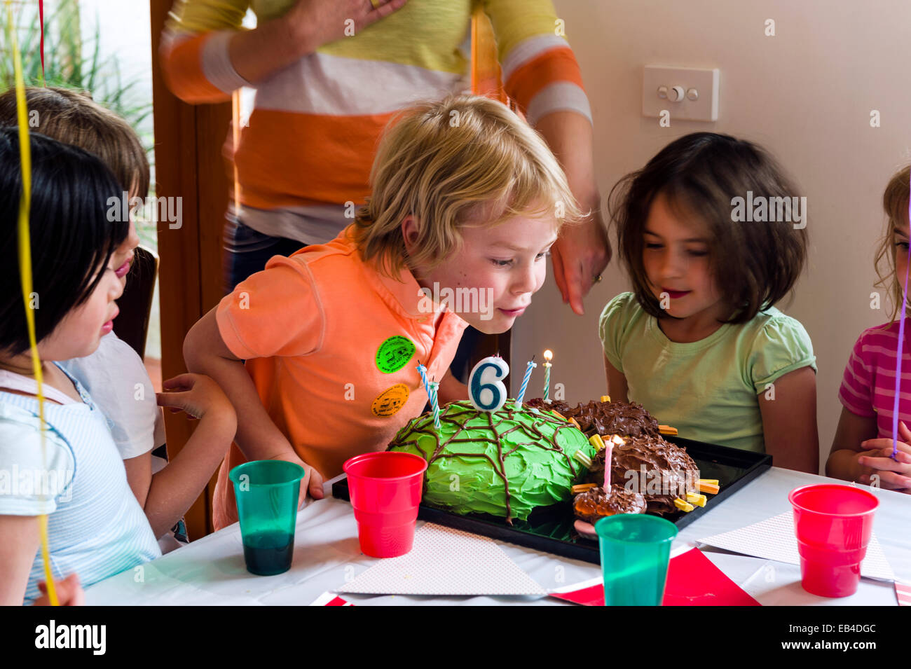 Un ragazzo soffiando fuori le candele sulla sua torta presso la sua festa di compleanno circondato dai suoi amici. Foto Stock