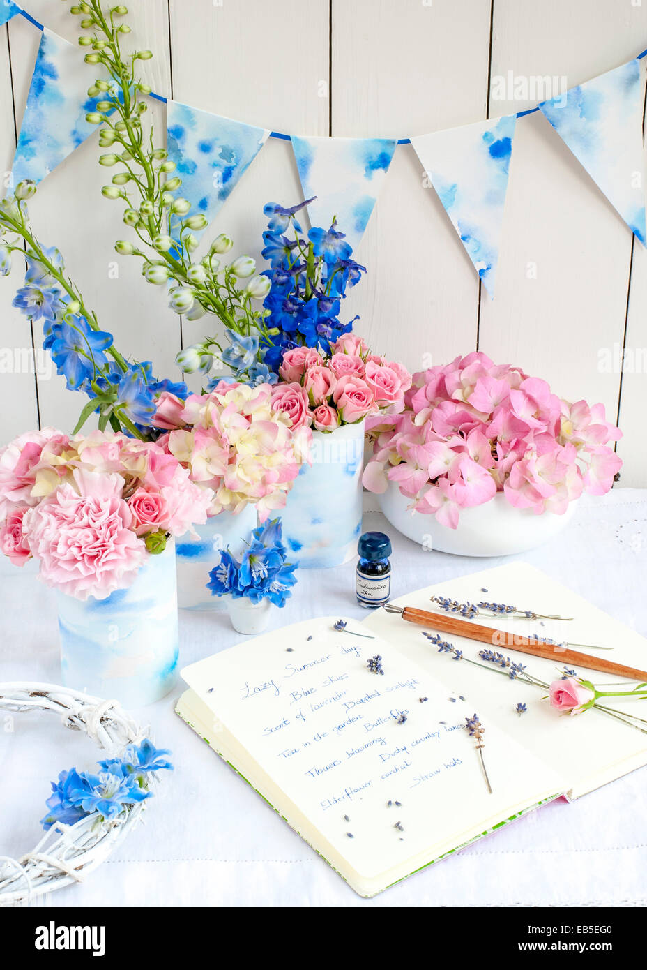 Notebook con note sull'estate, penna, inchiostro, lavanda, delphinium, rosa rose, garofani, ortensie, bunting, su sfondo bianco Foto Stock