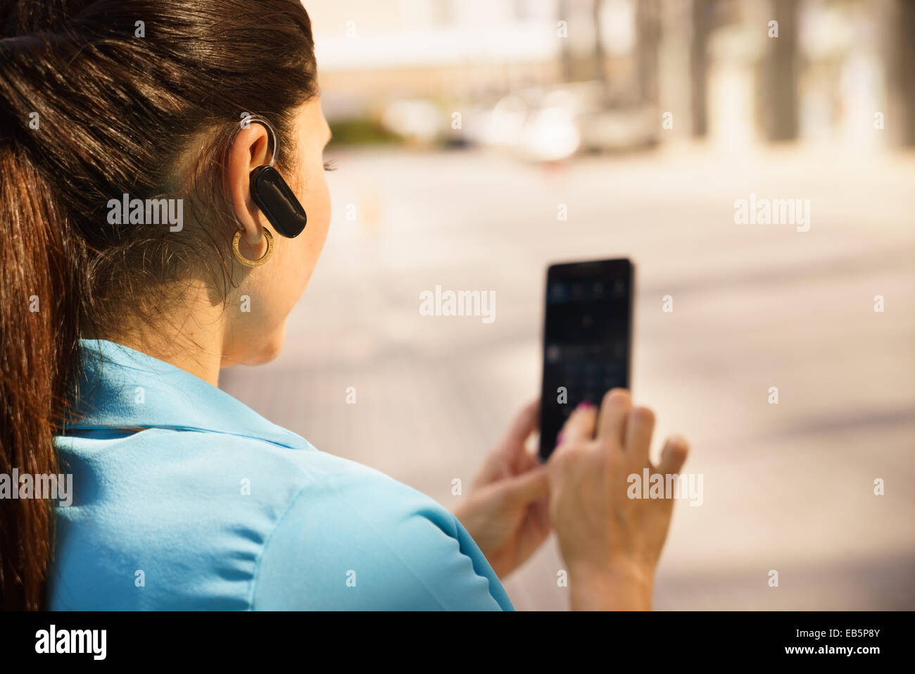 La metà degli adulti persona ispanica con il telefono cellulare e la cuffia auricolare Bluetooth di , digitare sul telefono in strada Foto Stock