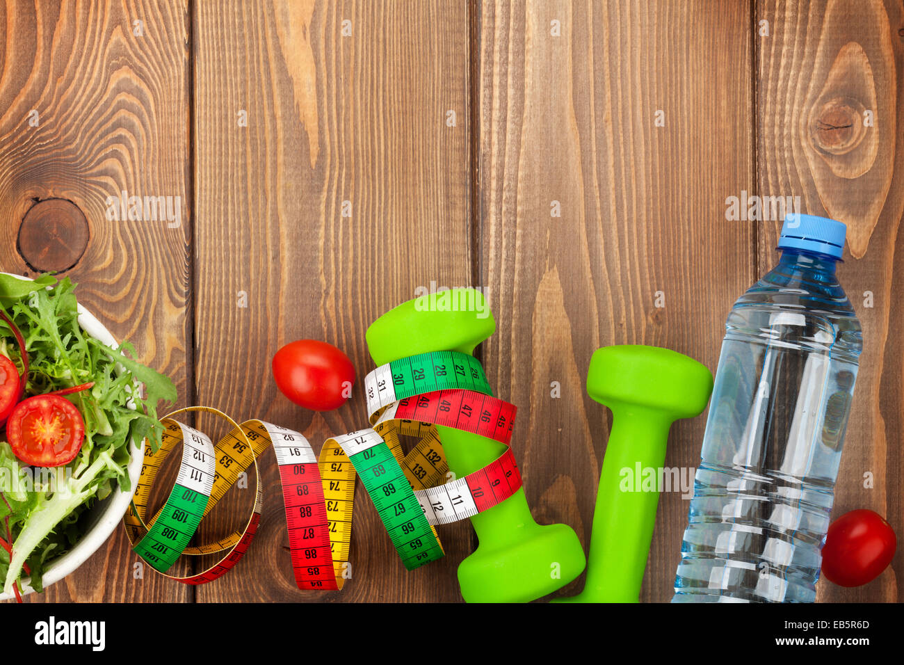 Manubri, metro a nastro e cibo sano su sfondo di legno. Fitness e salute. Vista da sopra con lo spazio di copia Foto Stock
