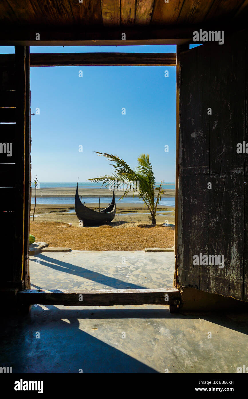 Guardando al di fuori della porta in una spiaggia con una barca da pesca e una noce di cocco Palm tree, In Cox bazar, Bangladesh Foto Stock