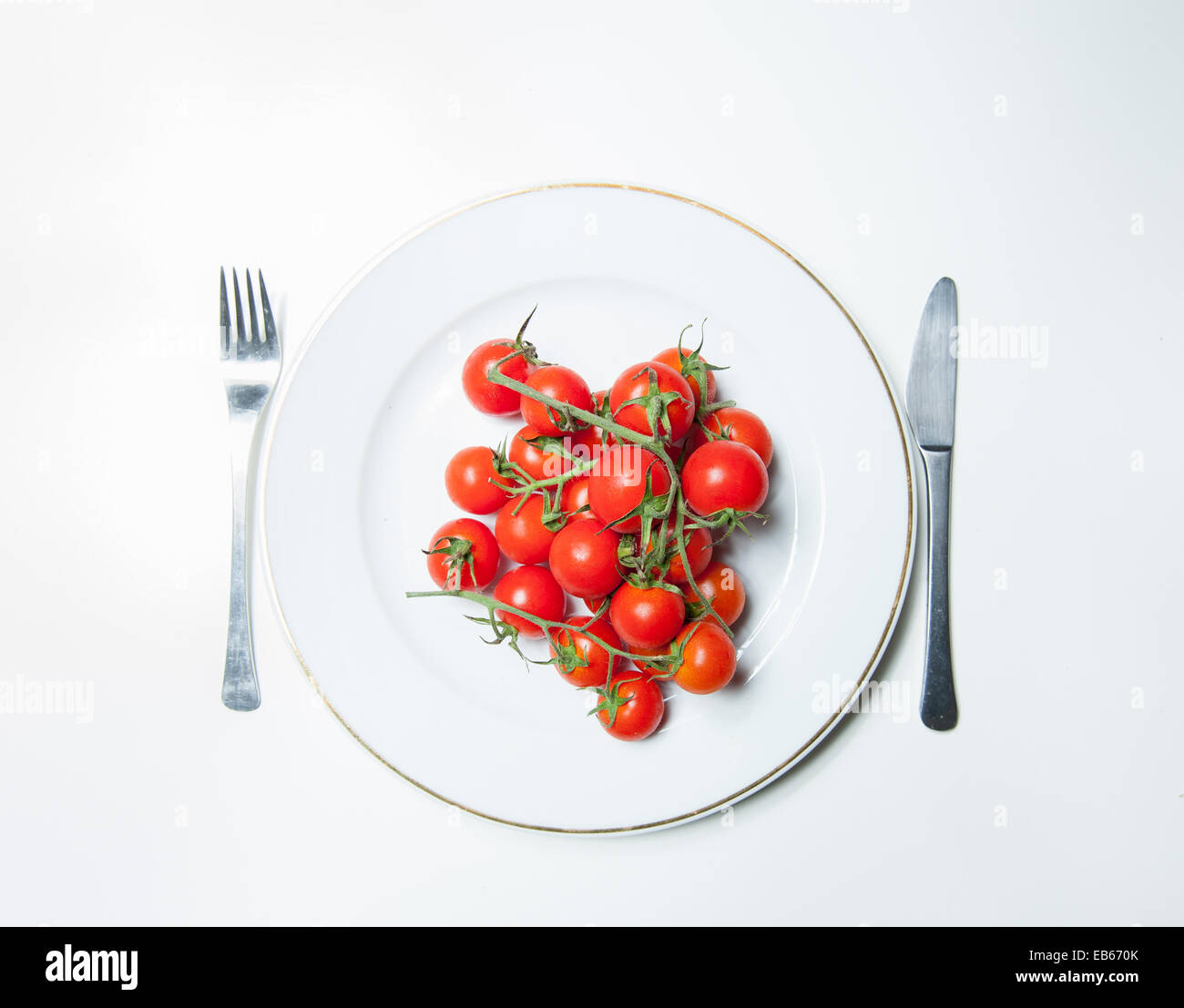 Crudo fresco di pomodori pachino classe su una piastra bianca con sfondo bianco con una forchetta e un coltello Foto Stock