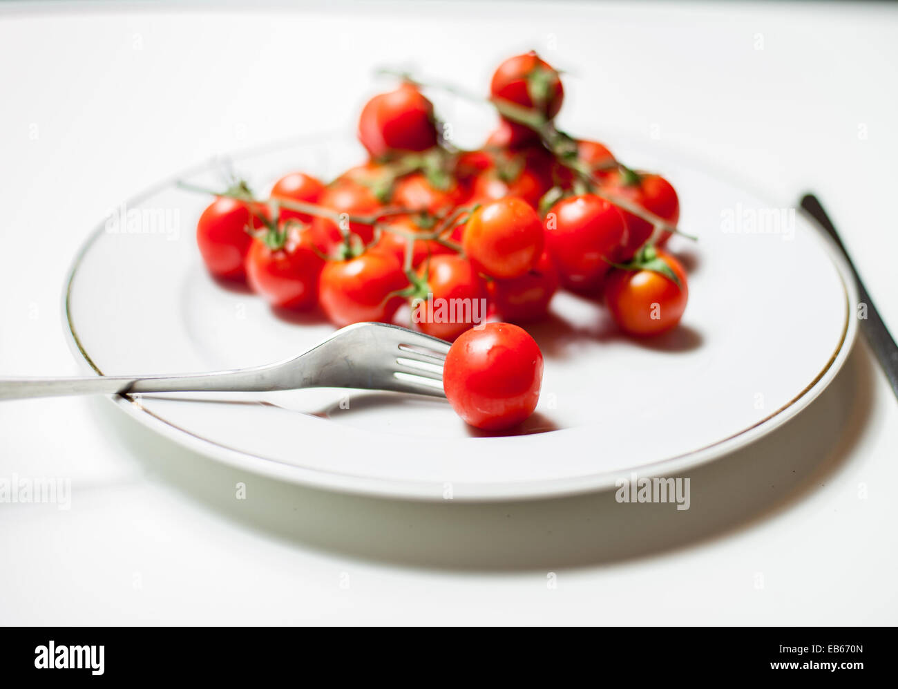 Dettaglio di un crudo fresco di pomodoro di Pachino classe su una piastra bianca con sfondo bianco con una forchetta e un coltello Foto Stock