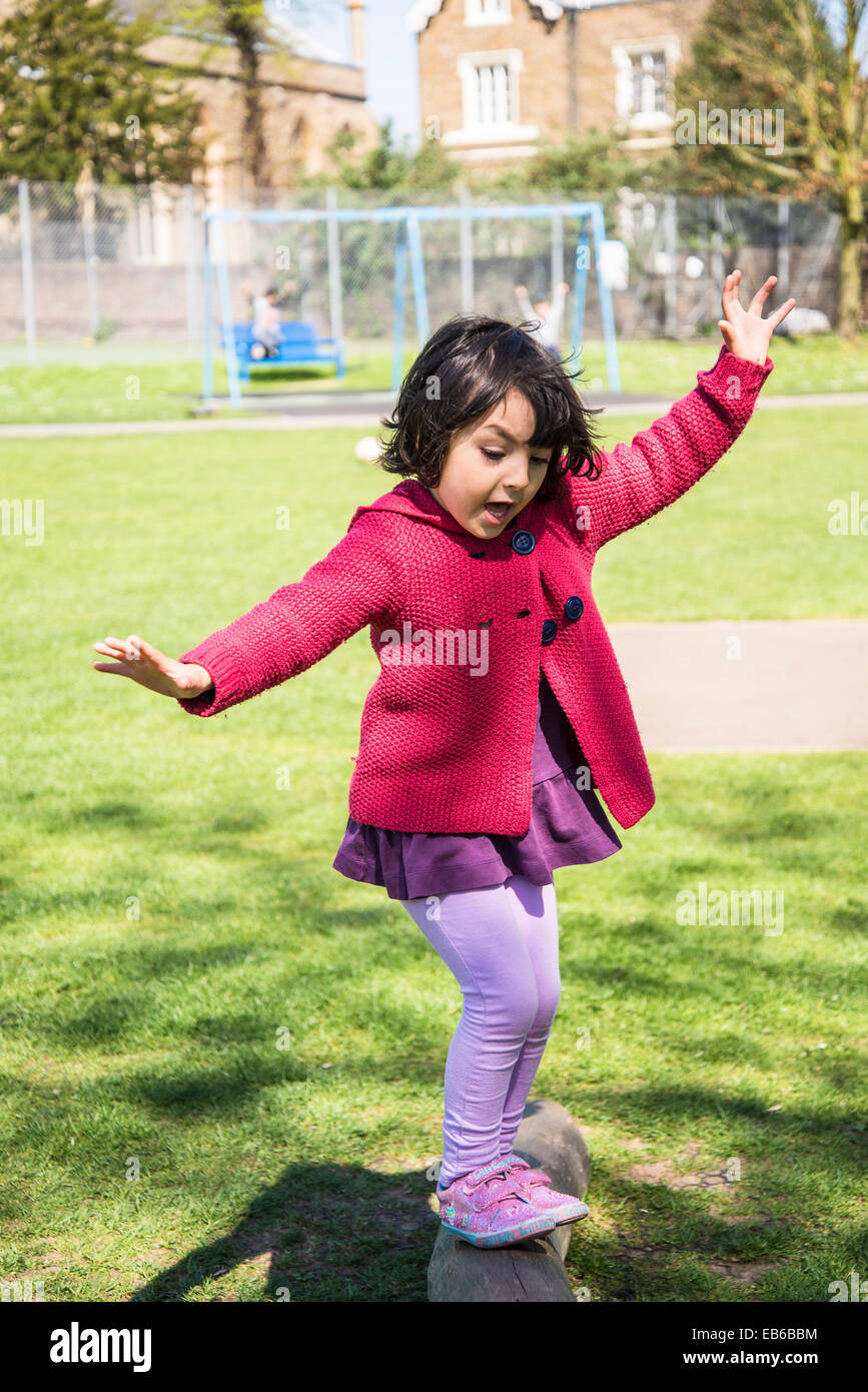 Bambina di cinque anni cercando di mantenere il suo equilibrio su una trave nel parco giochi per bambini Foto Stock