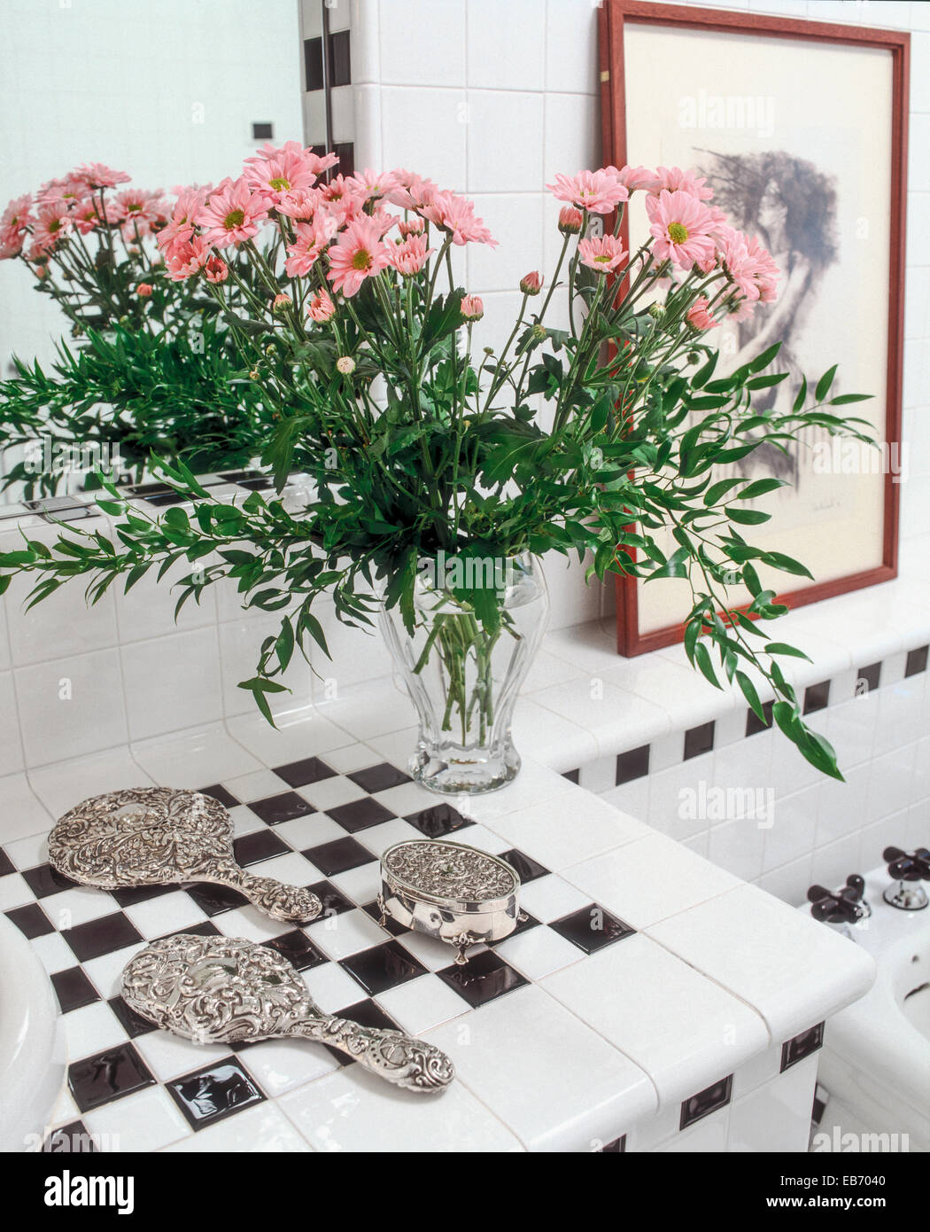 Oggetti in argento vicino al vaso di fiori di colore rosa sulla piastrella dal piano di lavoro nella stanza da bagno Foto Stock