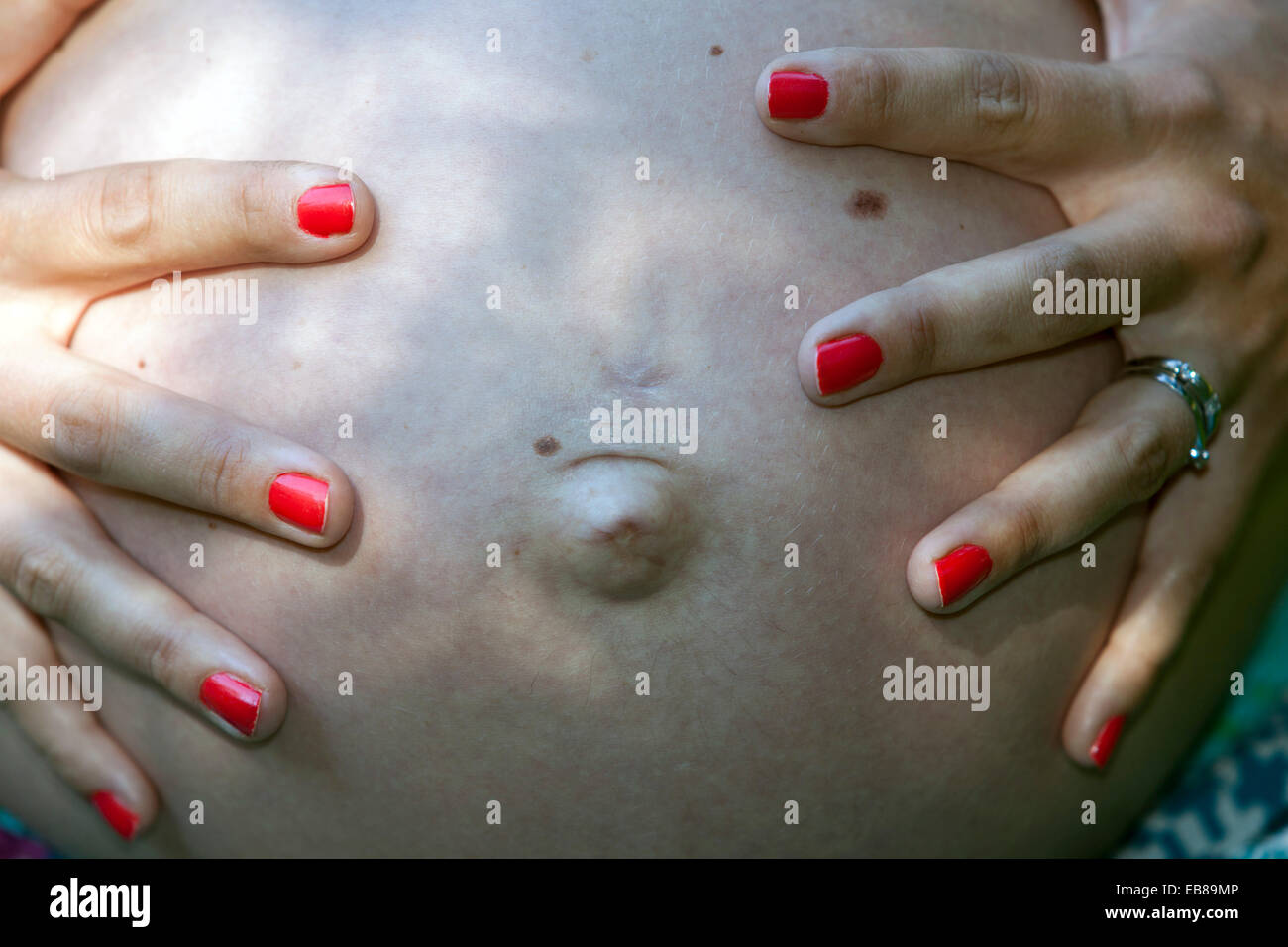 Pancia donna incinta, unghie dipinte di rosso, pancia incinta enorme Foto Stock