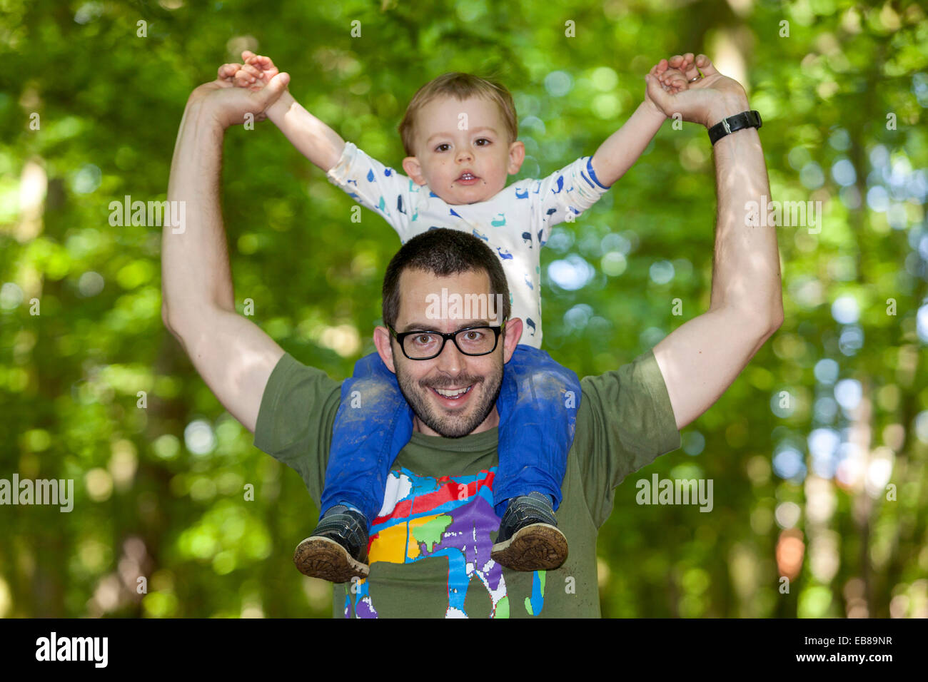 Padre felice che porta il figlio sulle spalle sotto la scena verde degli alberi Foto Stock