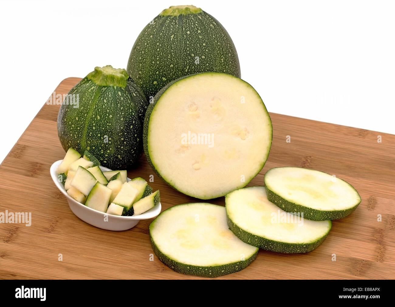 Round Le Zucchine affettate e tagliate su un pannello di legno con uno sfondo bianco Foto Stock