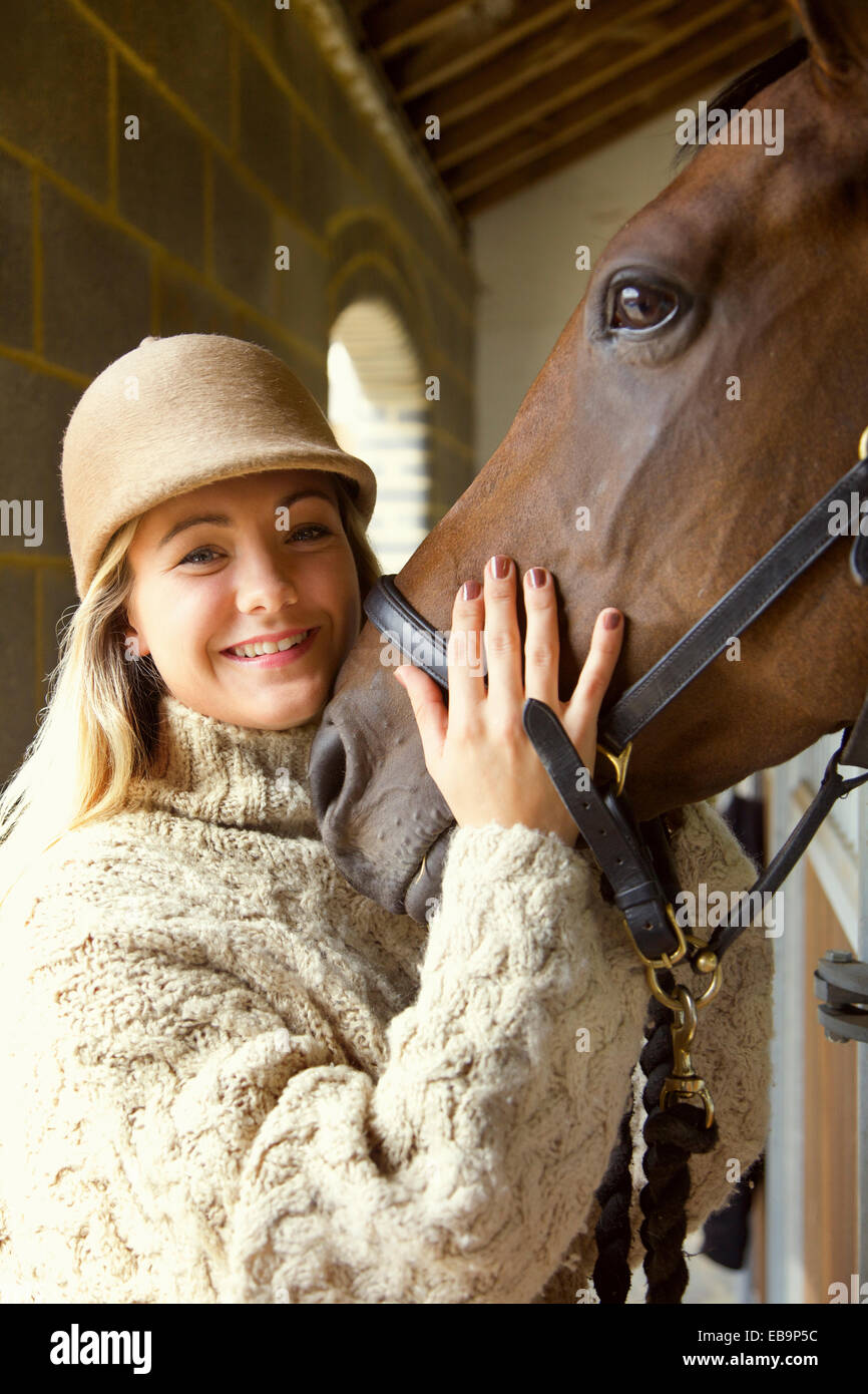 Sorridente giovane donna Stroking testa di cavallo Foto Stock