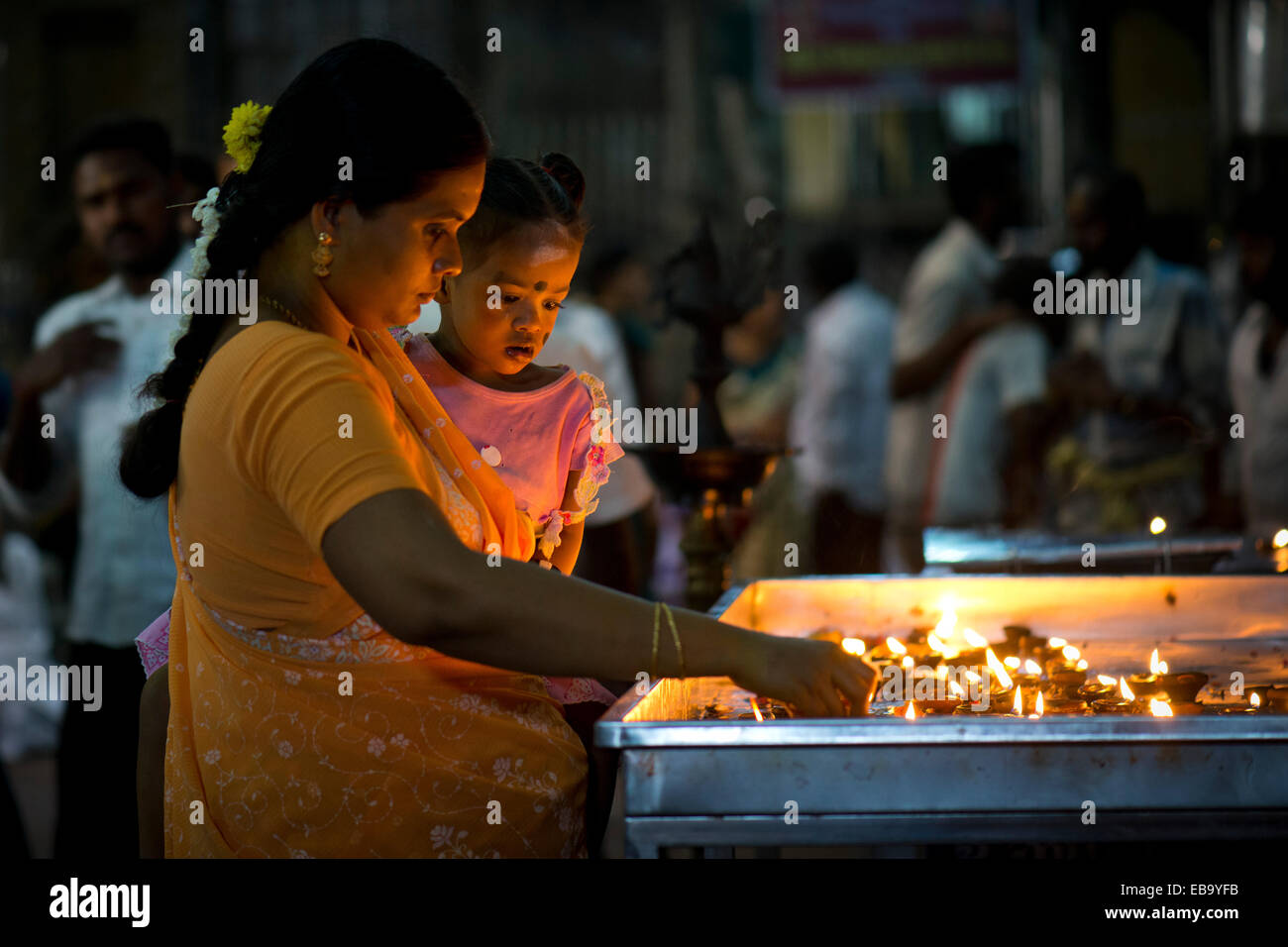 Donna che mantiene un bambino in braccio mentre l'illuminazione Lampade a olio in un tempio Meenakshi Amman Tempio o Sri Meenakshi Sundareswarar Foto Stock