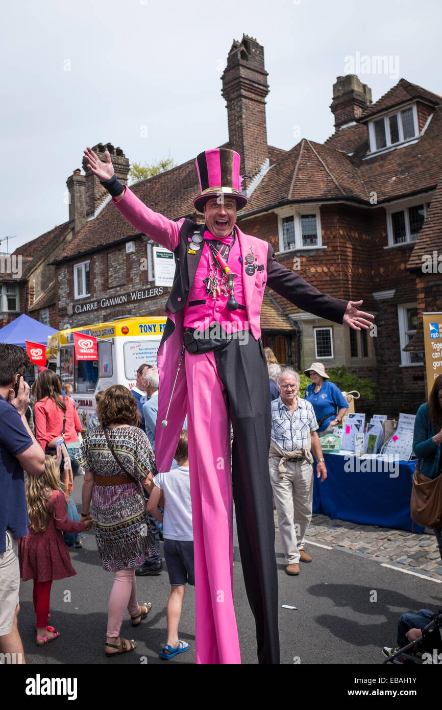 Animatore di strada su palafitte, indossando abiti luminosi e un top hat intrattiene la folla al Charter Fair Haslemere. Foto Stock