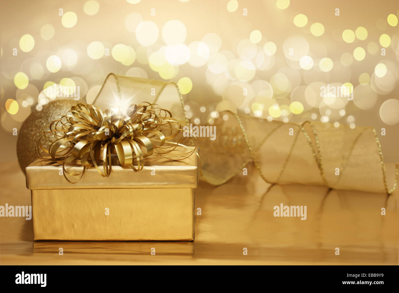 Golden sfondo di Natale con un regalo e luci bokeh di fondo Foto Stock