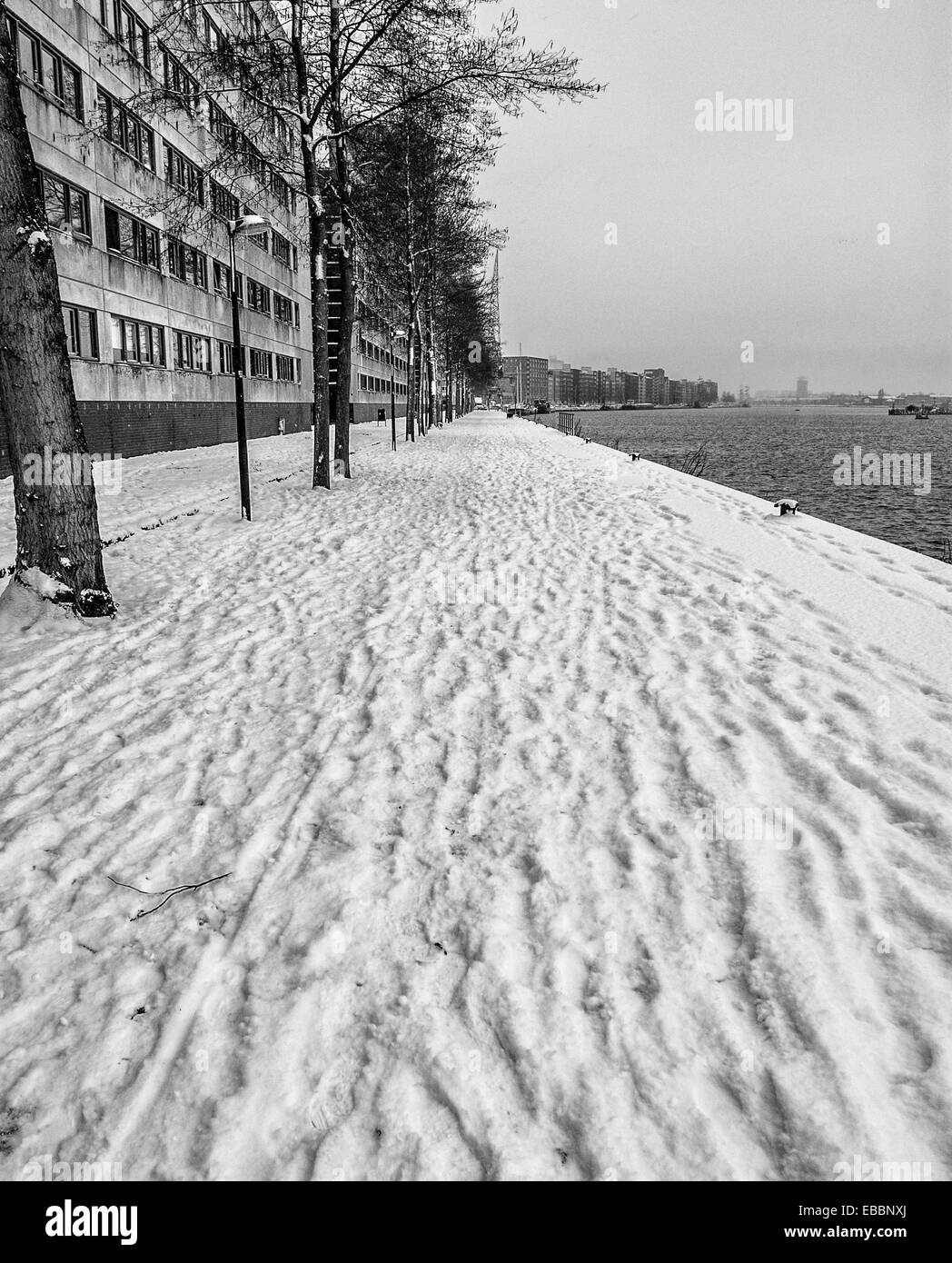 Coperta di neve quay nel porto di Amsterdam con tracce umane in bianco e nero Foto Stock