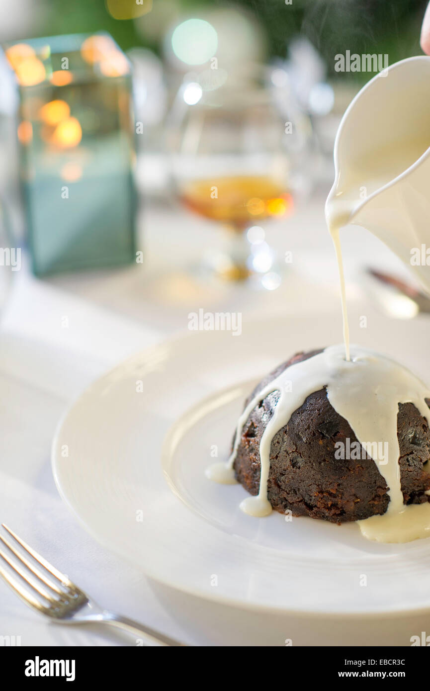 Pudding natalizio con crema che viene versato sopra la parte superiore. Foto Stock