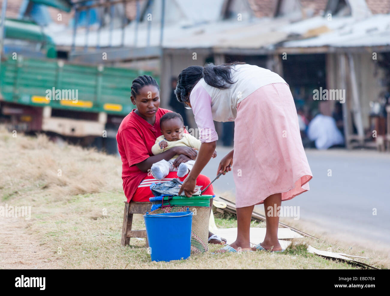 Locali africane donna con capelli briaded alimentando il suo paffuto bambino dal ciglio della strada, Antananariva, o Tana, la città capitale del Madagascar Foto Stock