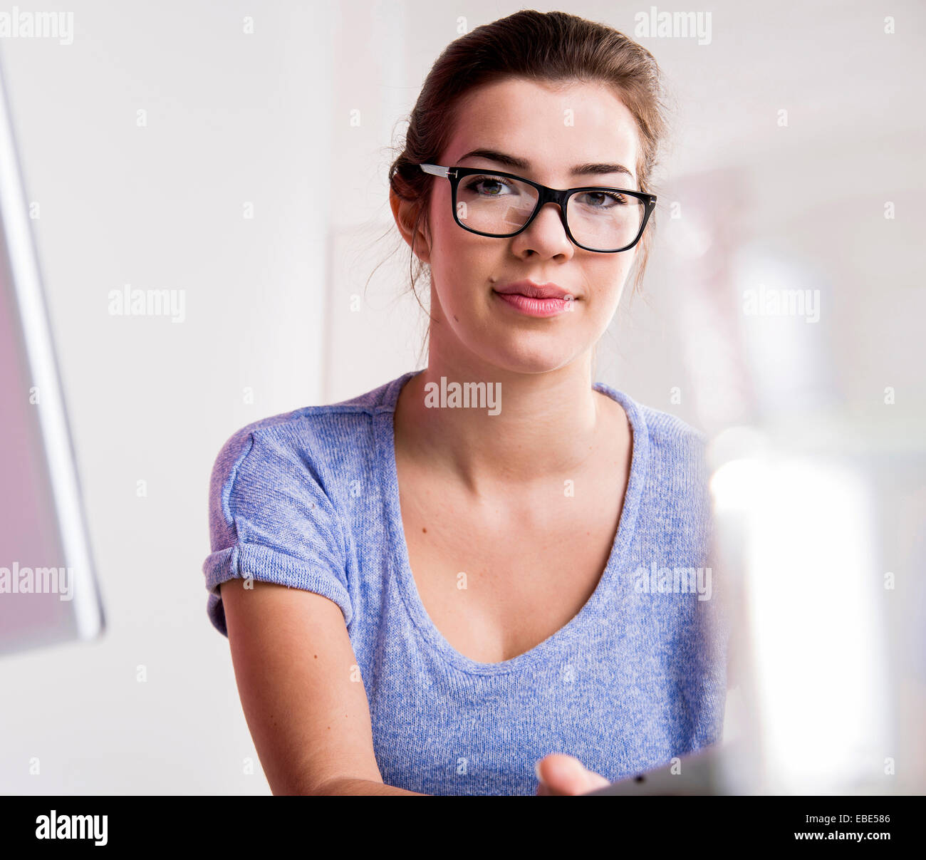 Ritratto di giovane donna in ufficio, indossando il corno-bordati di occhiali e guardando la telecamera, Germania Foto Stock