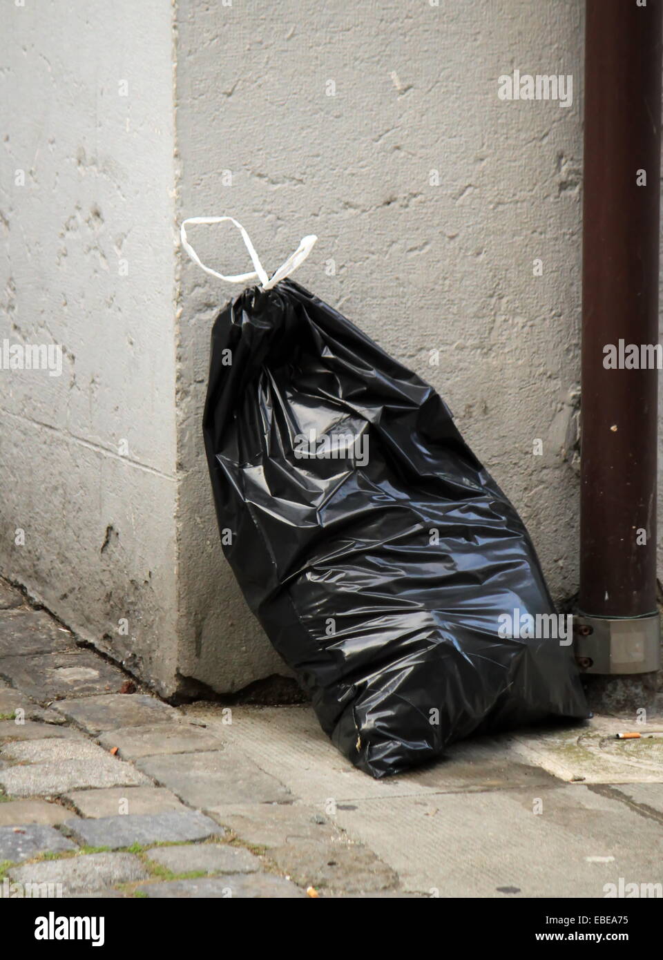 Uno nero garbage bag in strada contro una parete Foto Stock