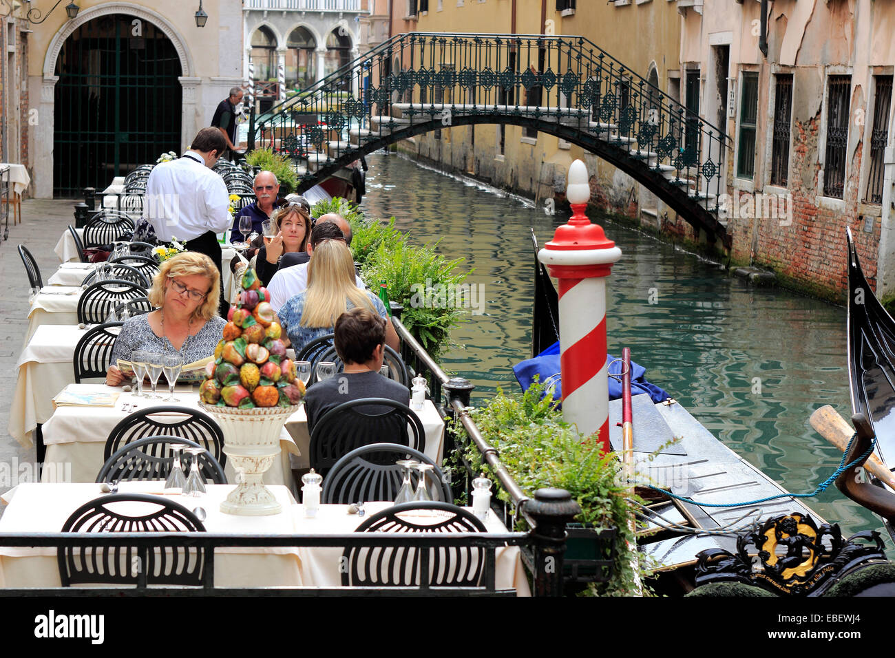 Venezia Sestiere San Marco un cameriere serve i turisti lungo un piccolo canale Foto Stock