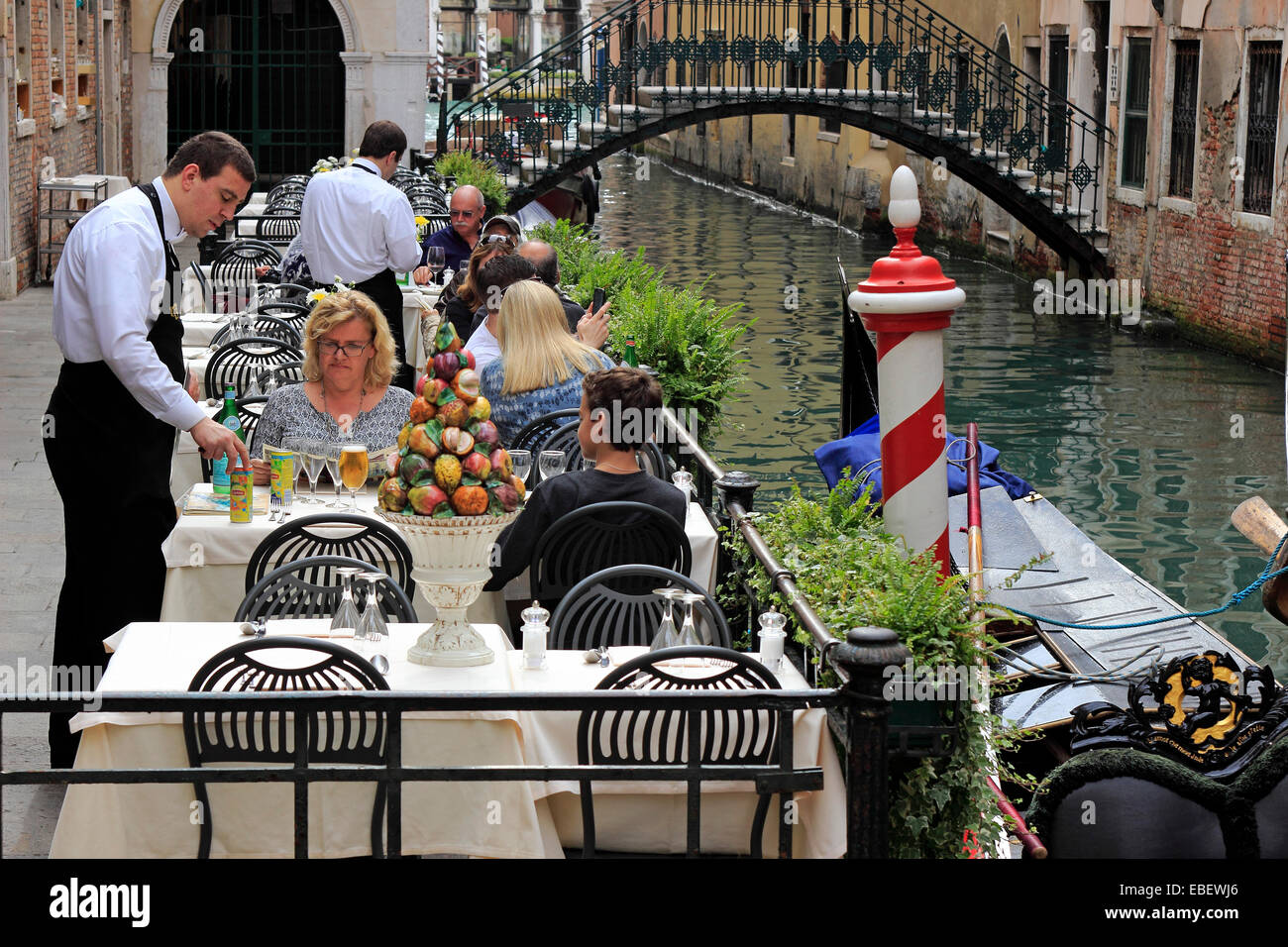 Venezia Sestiere San Marco un cameriere serve i turisti lungo un piccolo canale Foto Stock