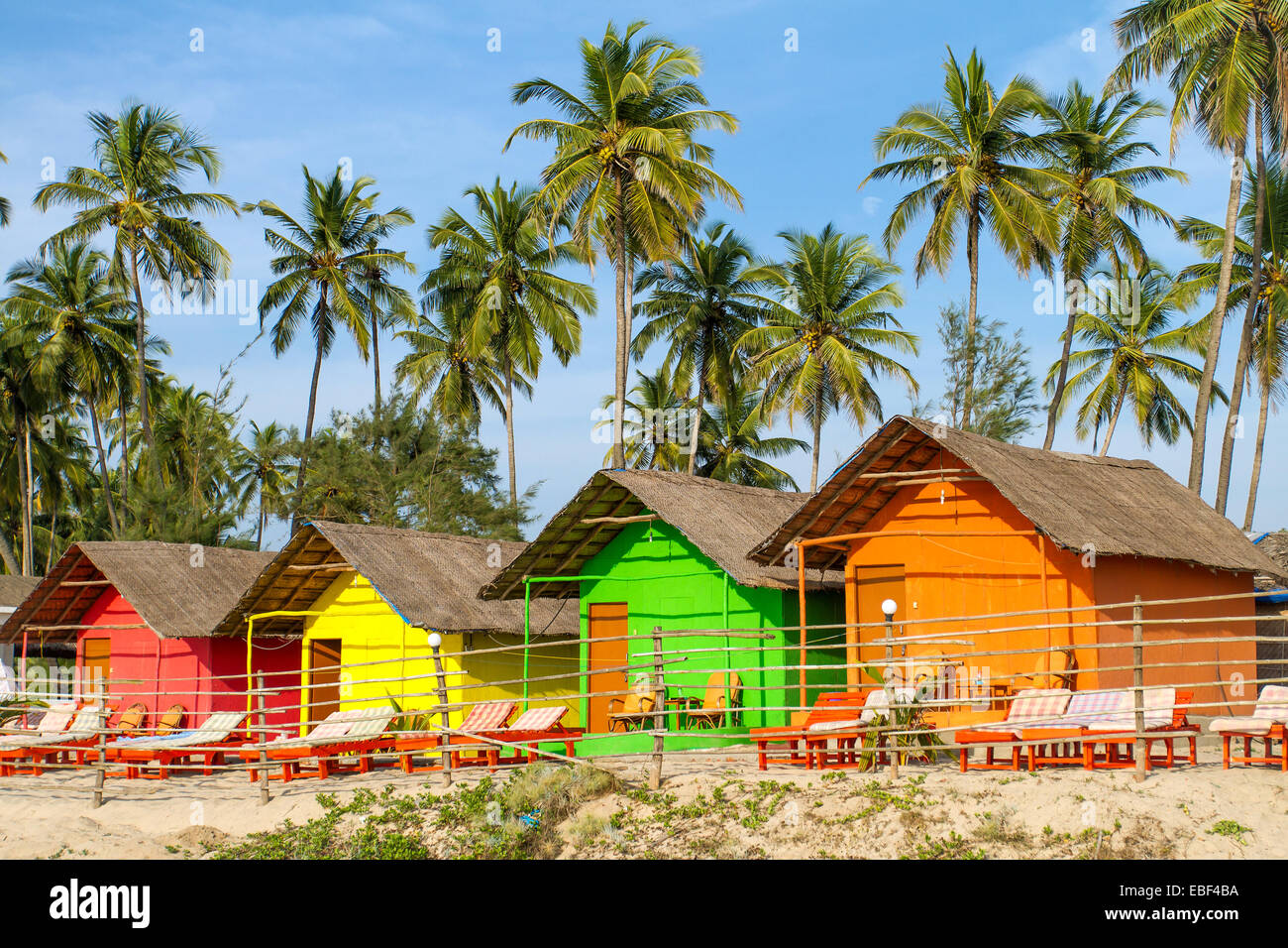 Capanne colorate sulla spiaggia sabbiosa con palme sfondo in Goa, India Foto Stock