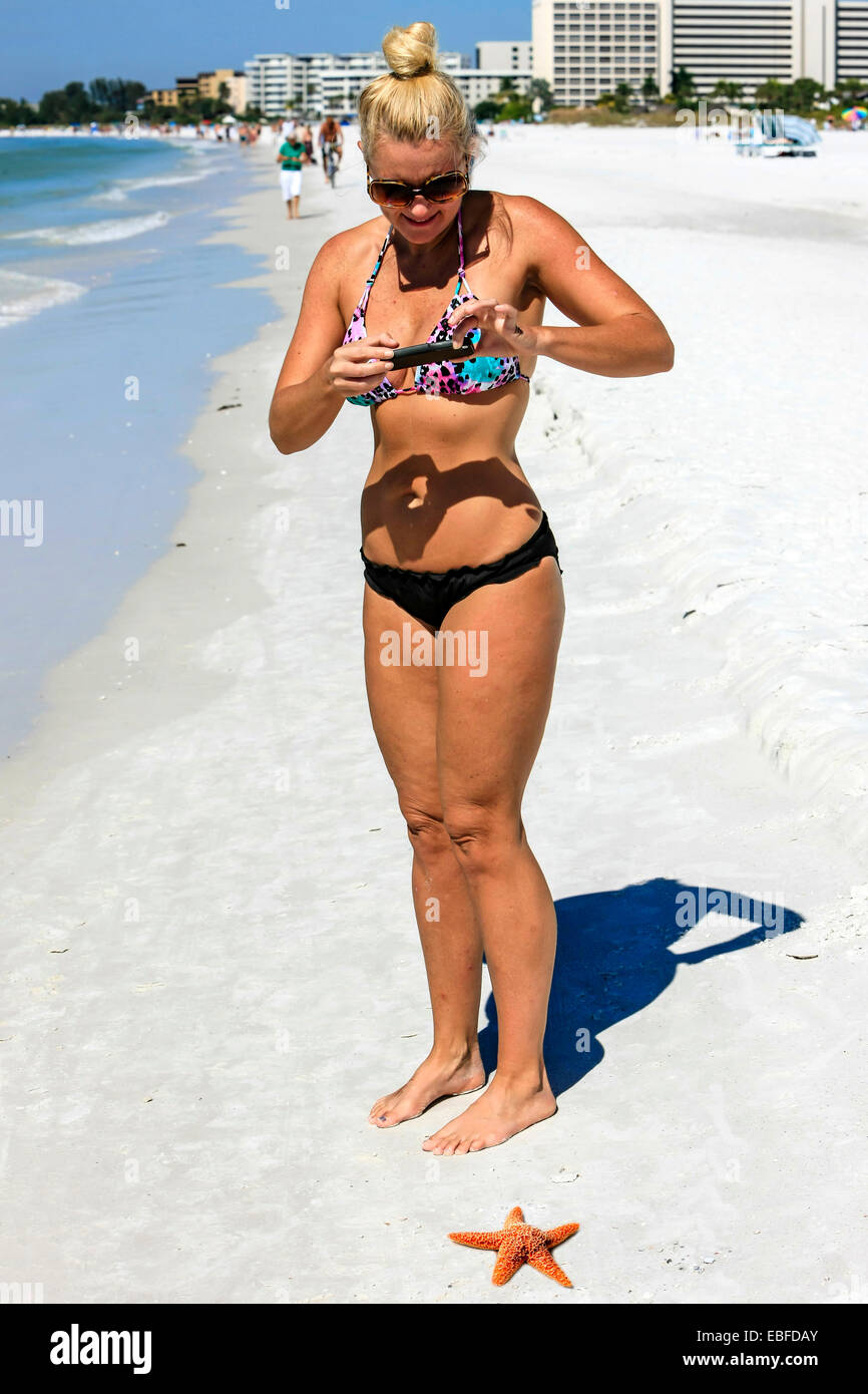 Una giovane donna assume una foto con il suo iPhone di una stella di mare sulla spiaggia a mezzaluna su Siesta Key isola in Sarasota FL Foto Stock