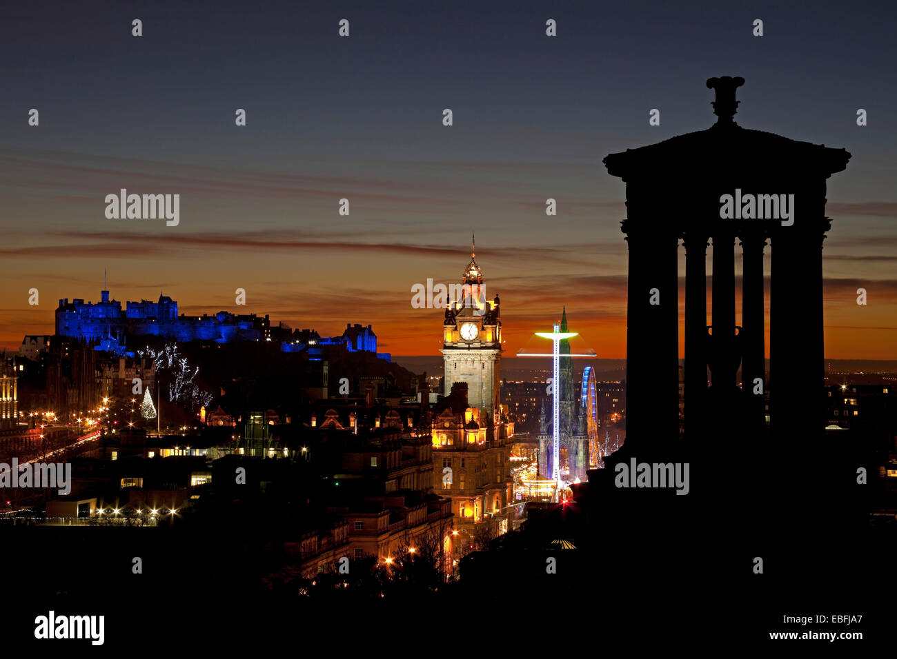 Edimburgo, Scozia, Regno Unito. 30 Novembre, 2014. Il Castello di Edinburgo e la città vista da Calton Hill al tramonto il castello viene illuminato con luce blu durante il St Andrew's Day celebrazioni, che mostra anche la grande ruota e Star Flyer rides situato accanto al Monumento di Scott nei giardini di Princes Street East. Foto Stock