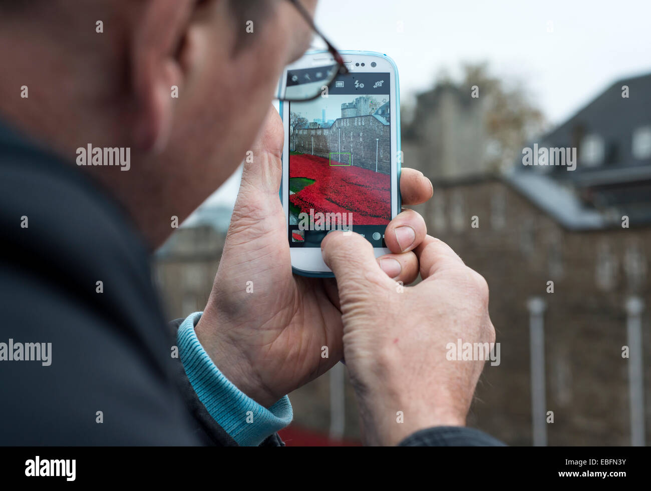 Uomo che utilizza un telefono cellulare per scattare una fotografia dei papaveri presso la Torre di Londra, Inghilterra, Regno Unito Foto Stock