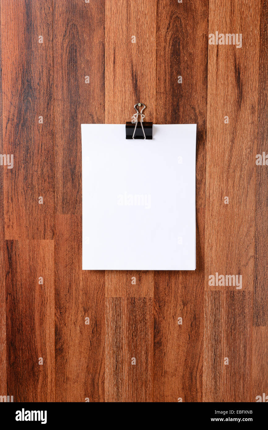 I fogli bianchi di carta trattenuta da un fermo appeso a un chiodo nel mezzo di un legno scuro muro. Formato verticale. La schermata bianca vuota pap Foto Stock
