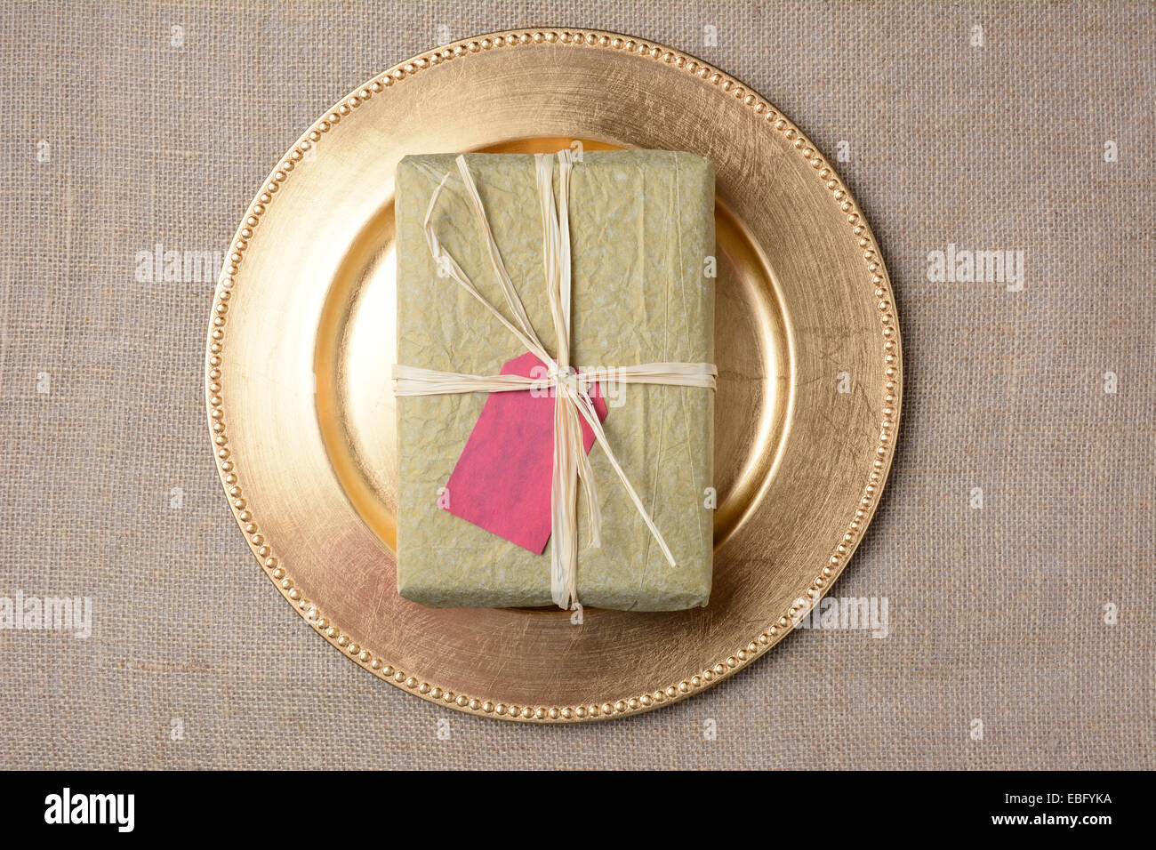 Alta angolazione di un tessuto di carta avvolto il Natale presente su un caricabatteria oro su una tela ruvida la superficie. Il dono è un fustellato tag regalo Foto Stock