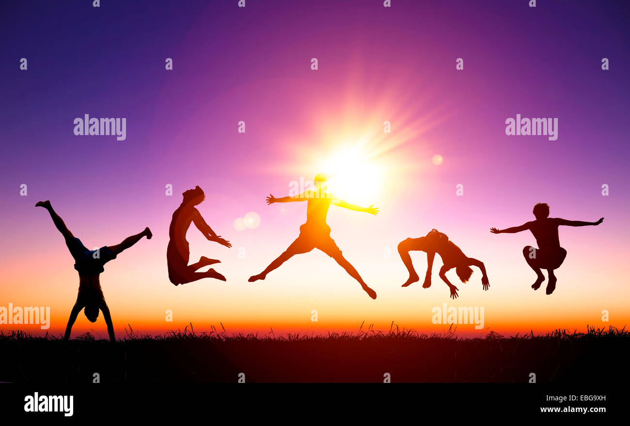 Felice giovani saltando su di una collina con la luce del sole sullo sfondo Foto Stock