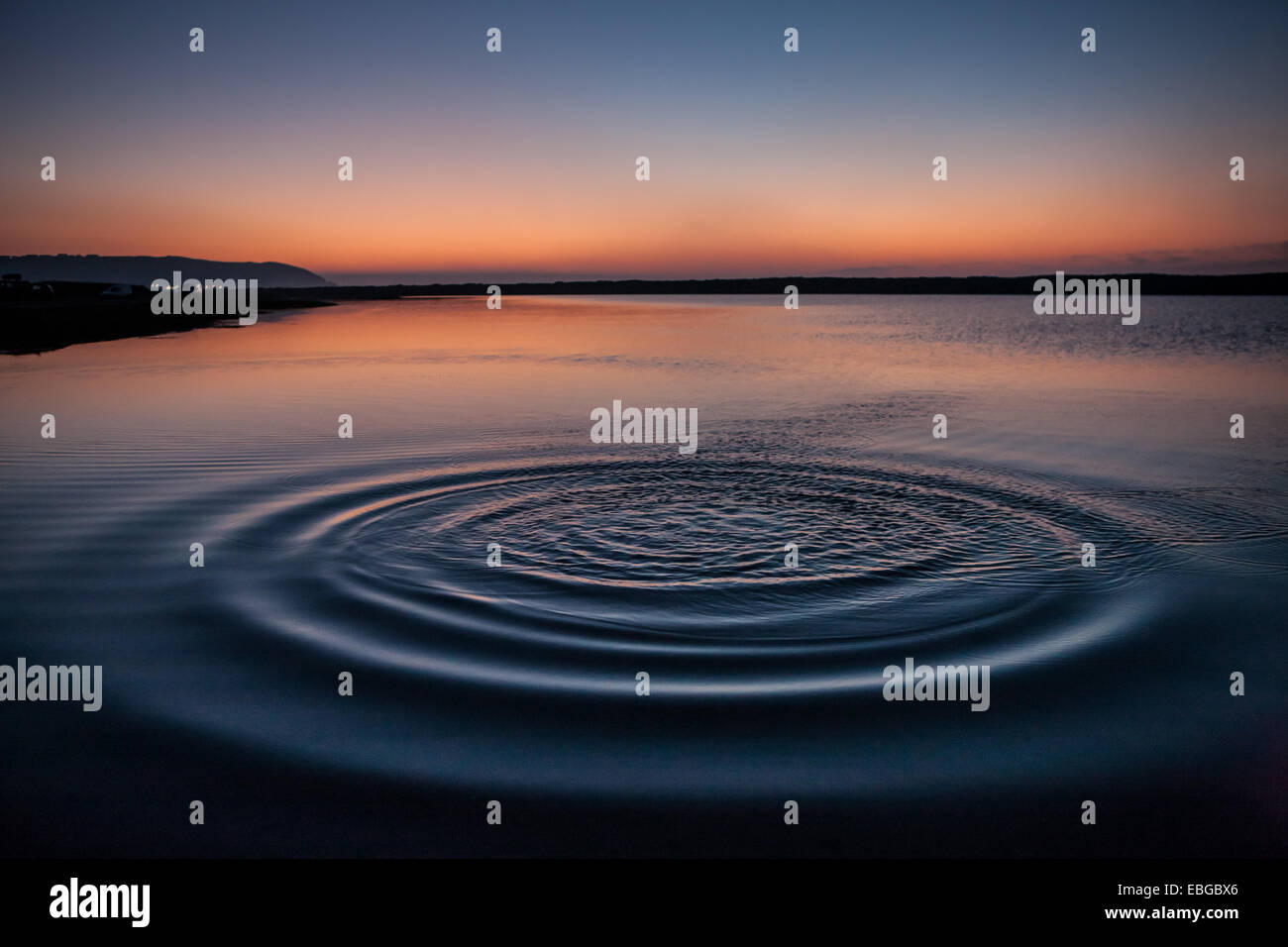 La sempre maggiore diffusione delle increspature da dove un ciottolo è stato gettato in acque calme a Westward H Foto Stock