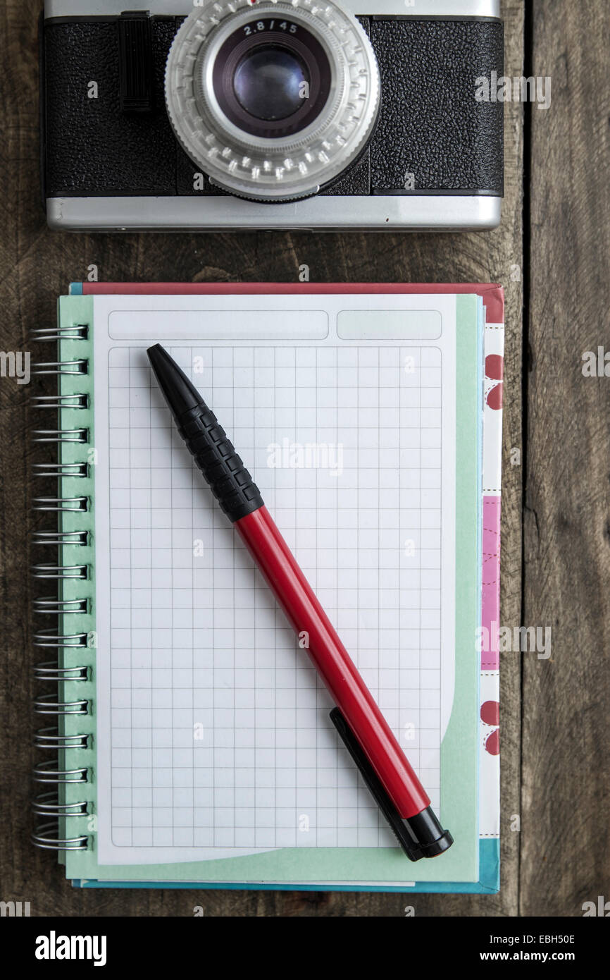 Blank notebook con penna e fotocamera retrò sul tavolo di legno, vista aerea. Foto Stock