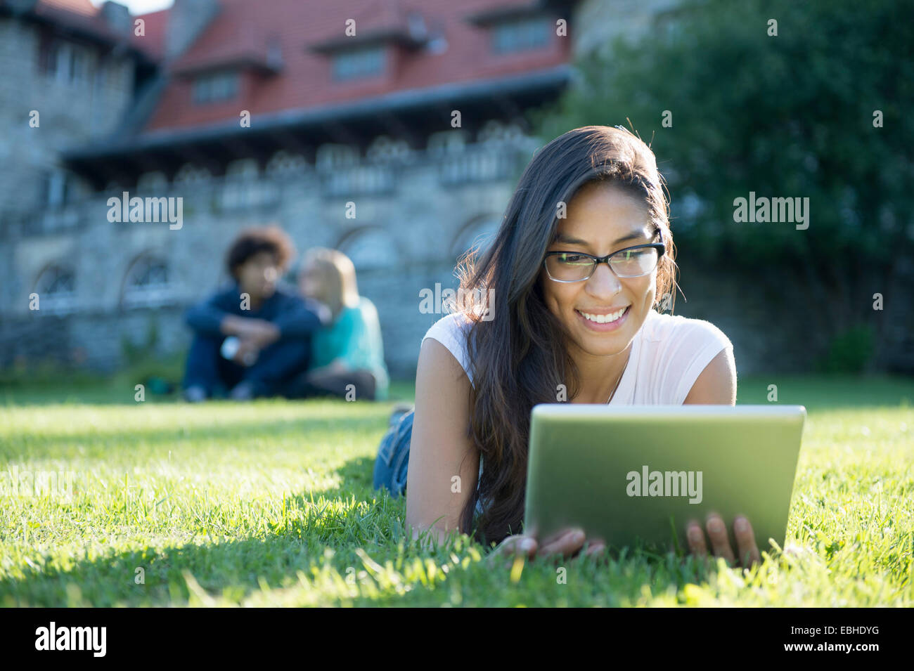 Giovane donna sdraiata su erba usando tavoletta digitale Foto Stock