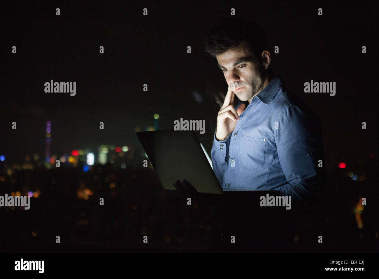 Giovane imprenditore guardando portatile nella parte anteriore del grattacielo Finestra di ufficio di notte, Shanghai, Cina Foto Stock