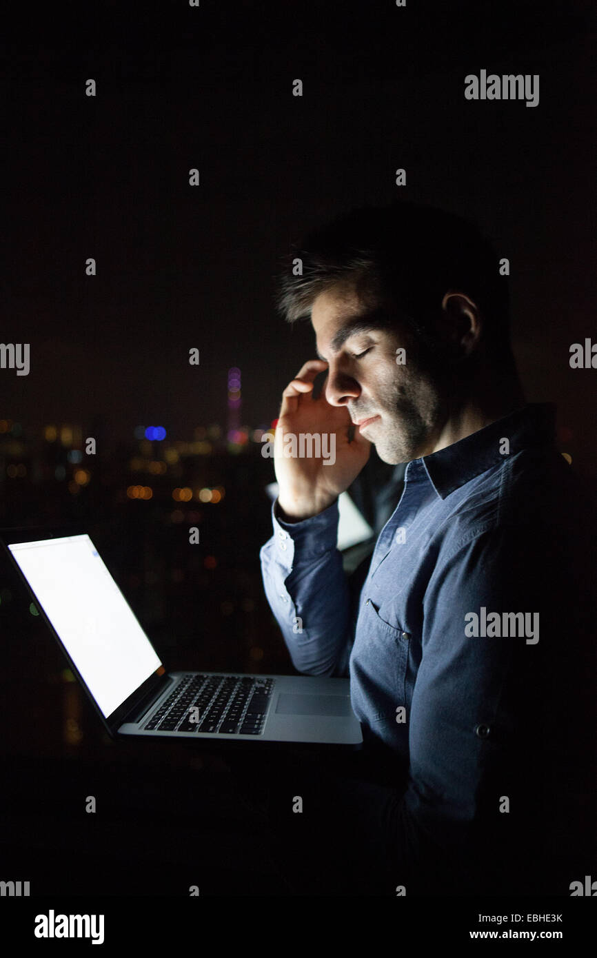 Stanco giovane uomo d affari con computer portatile nella parte anteriore del grattacielo Finestra di ufficio di notte, Shanghai, Cina Foto Stock