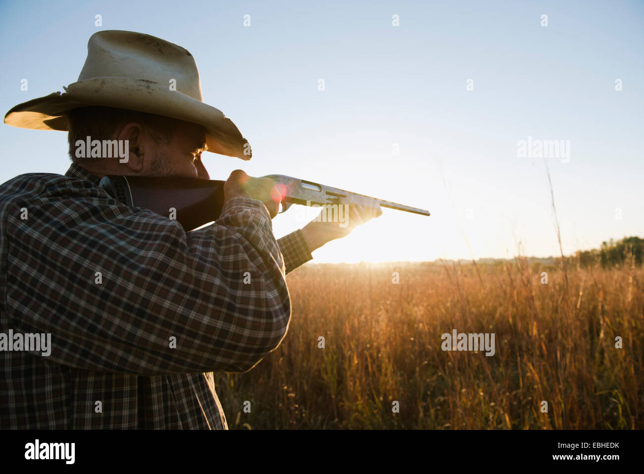 Anziano agricoltore maschile che mira fucile da caccia in campo al crepuscolo, Plattsburg, Missouri, Stati Uniti Foto Stock