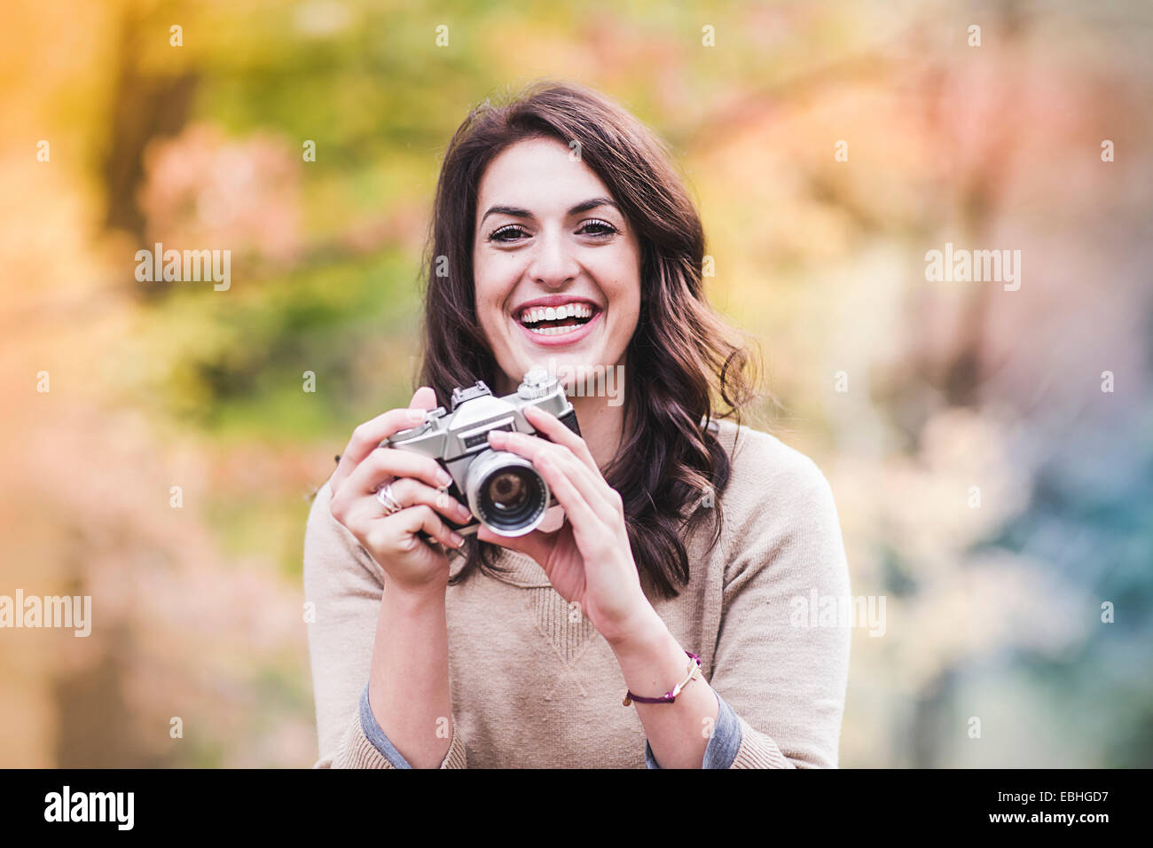 Ritratto di sorridente giovane donna con fotocamera reflex in foresta di autunno Foto Stock