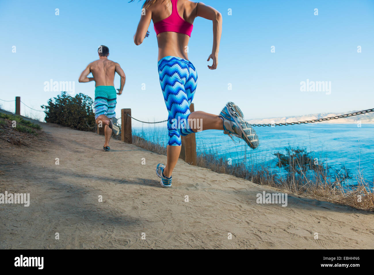 Metà uomo adulto e giovane donna in esecuzione sul percorso dal mare, vista posteriore Foto Stock