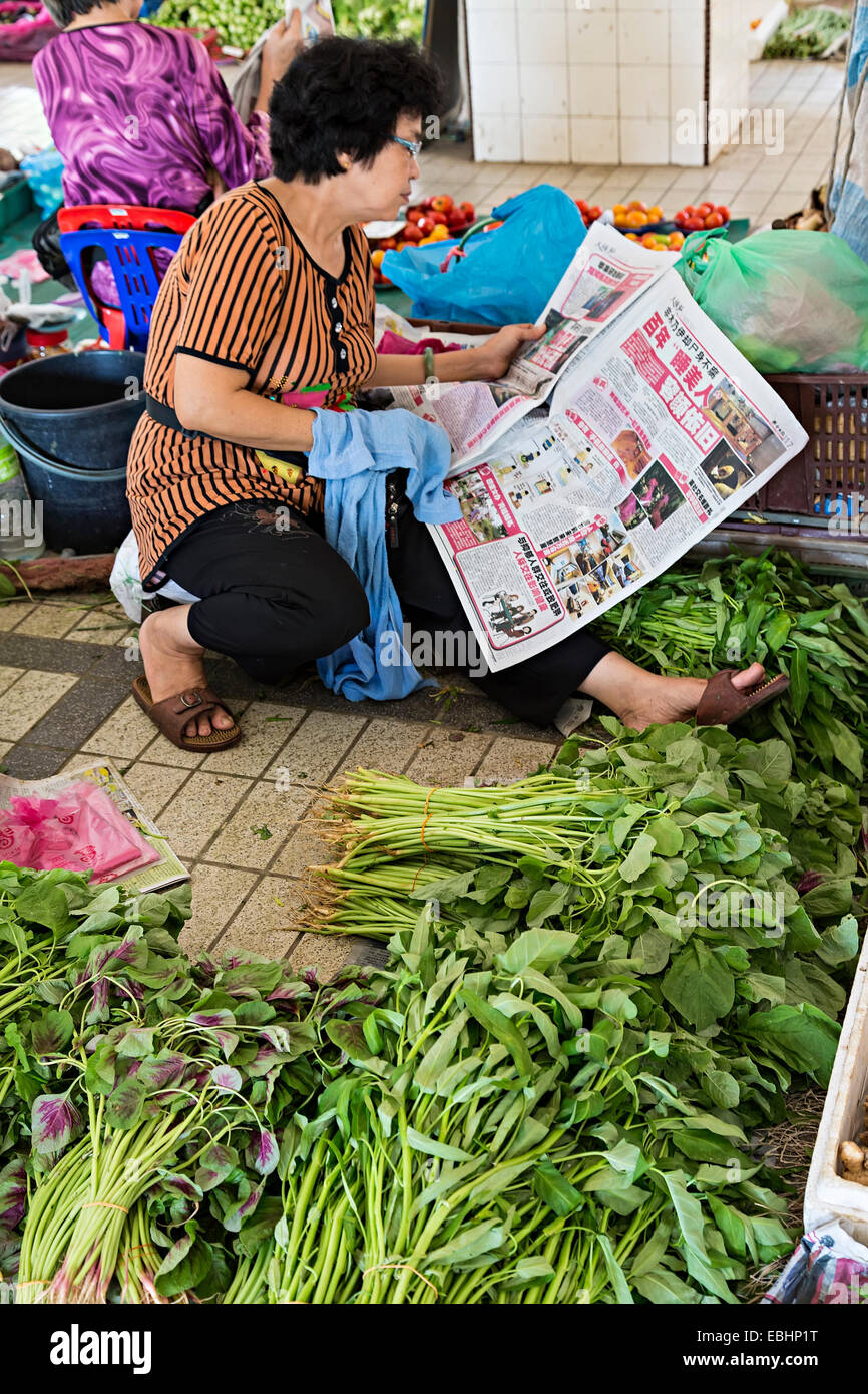 Donna che legge il giornale la vendita di produrre nel mercato, Miri, Malaysia Foto Stock